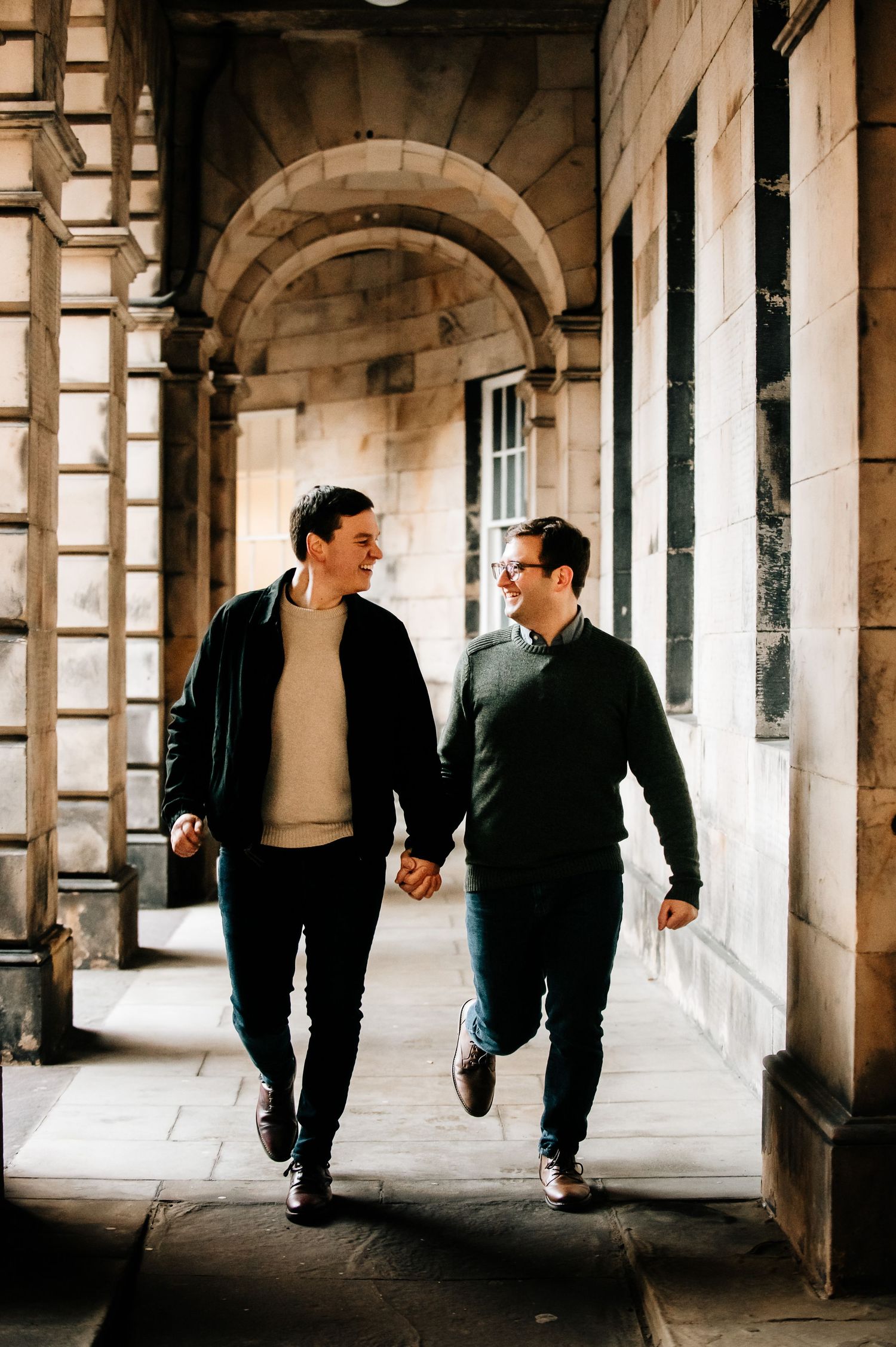 Two people walking hand in hand through an elegant stone archway corridor.