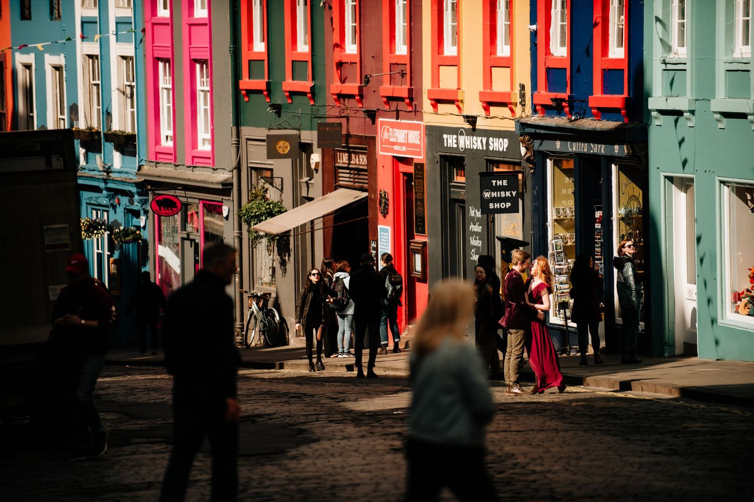 Colourful row of historic buildings with bright pink, blue, and red facades line Victoria Street, Edinburgh.