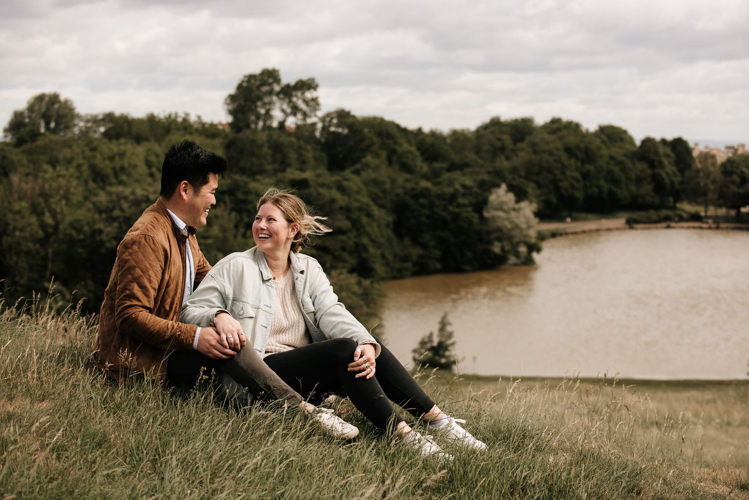 Two people relaxing by a serene lake on a grassy hillside.