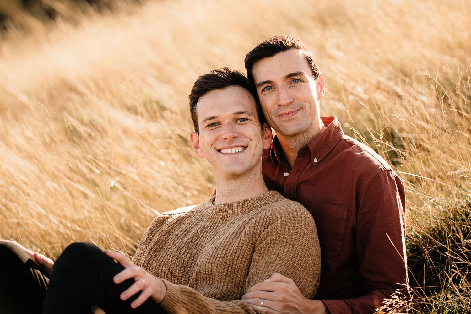 A couple shares an intimate moment while sitting in sunlit golden grass.