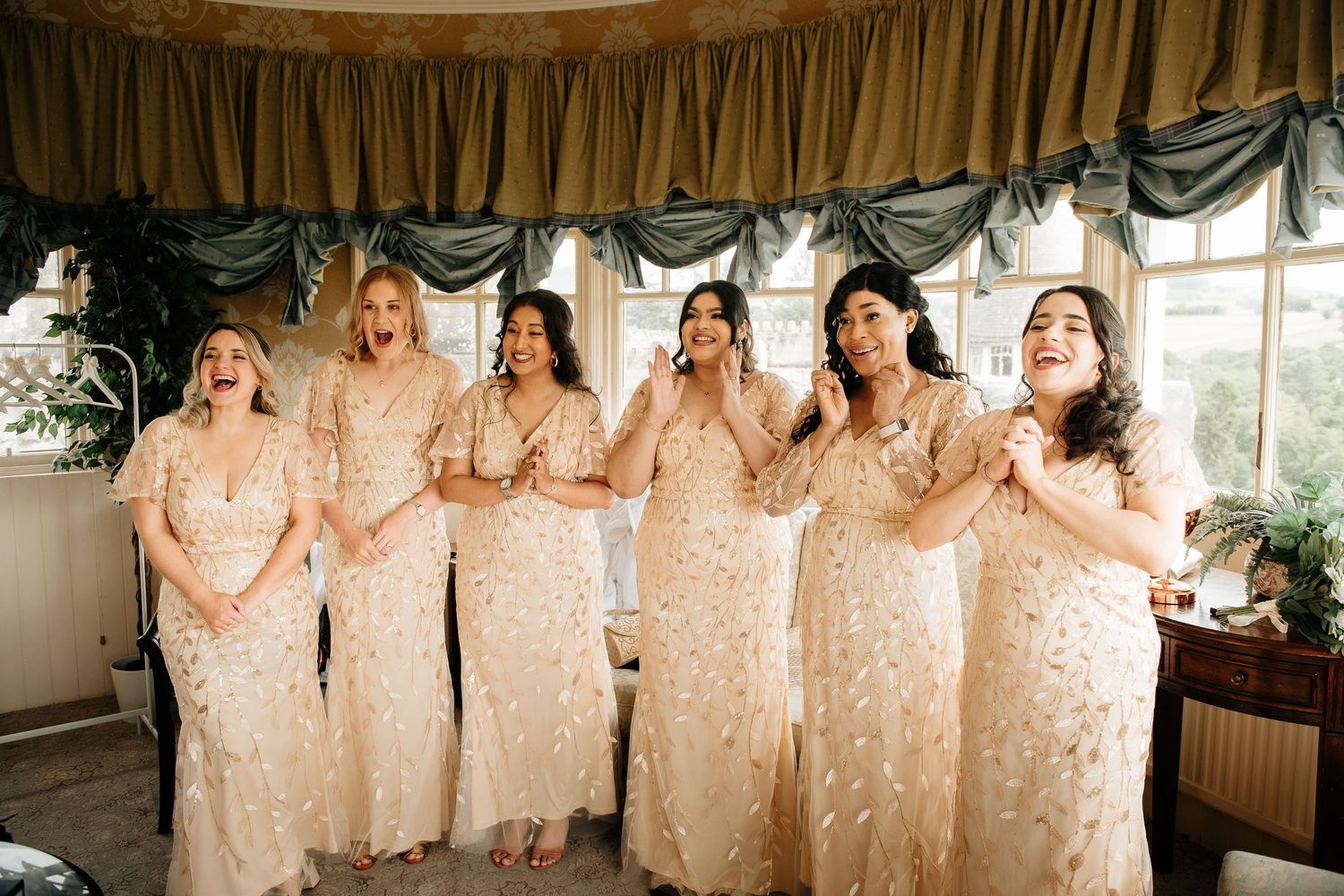 Row of bridesmaids in matching champagne colored dresses posing together.