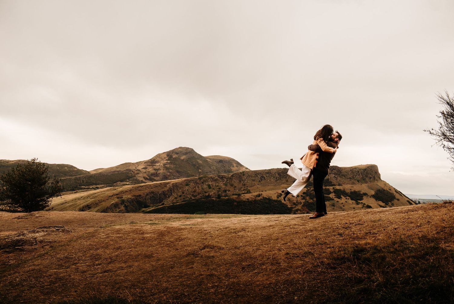 Scenic hilltop engagement photography session with Edinburgh's dramatic landscape in the background.