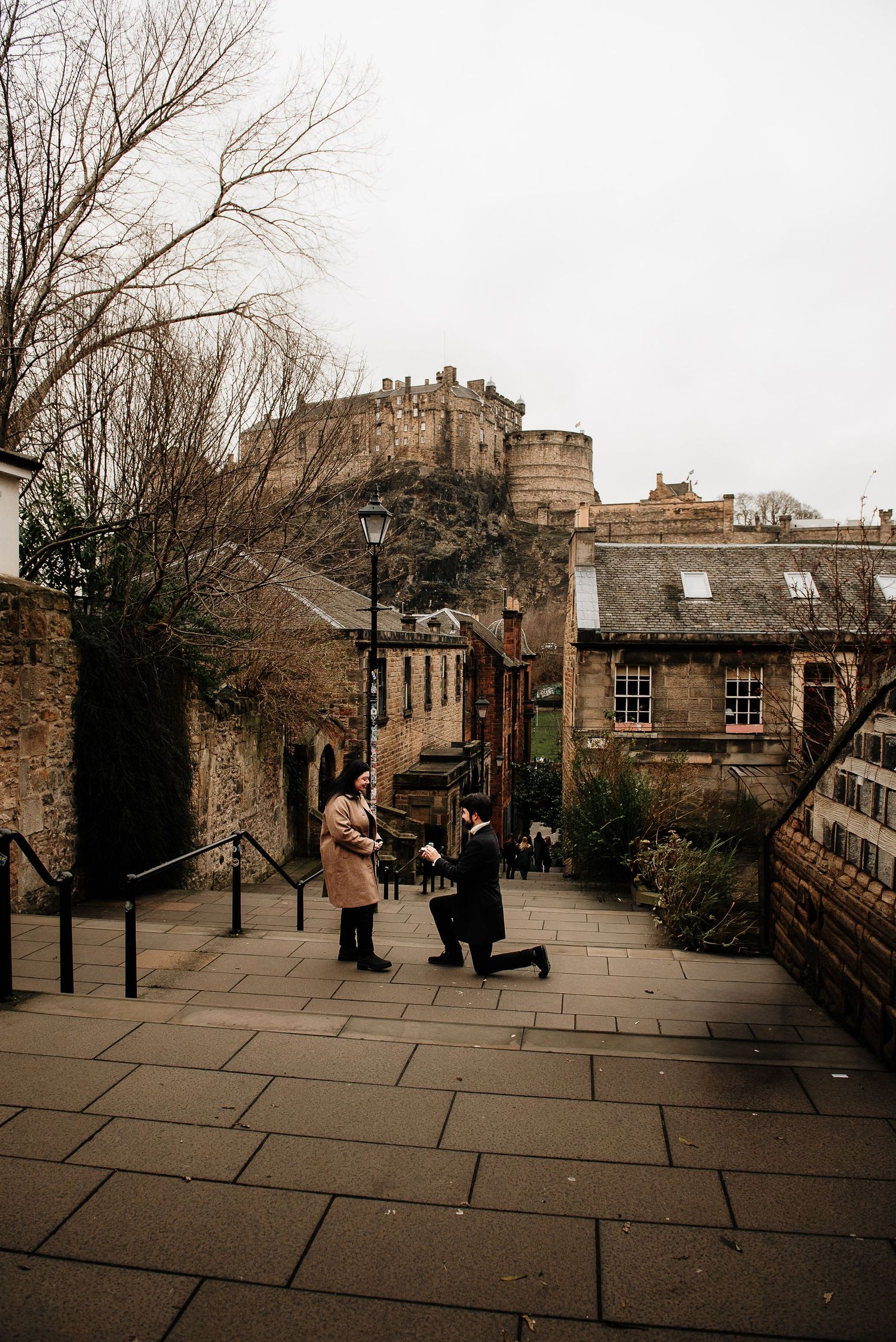 Proposal scene on cobblestone street with Edinburgh Castle looming in background.