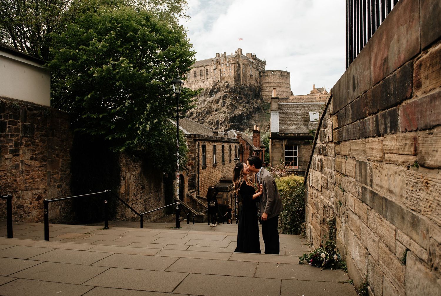 A couple shares a quiet moment on stone steps with Edinburgh Castle dominating the backdrop.