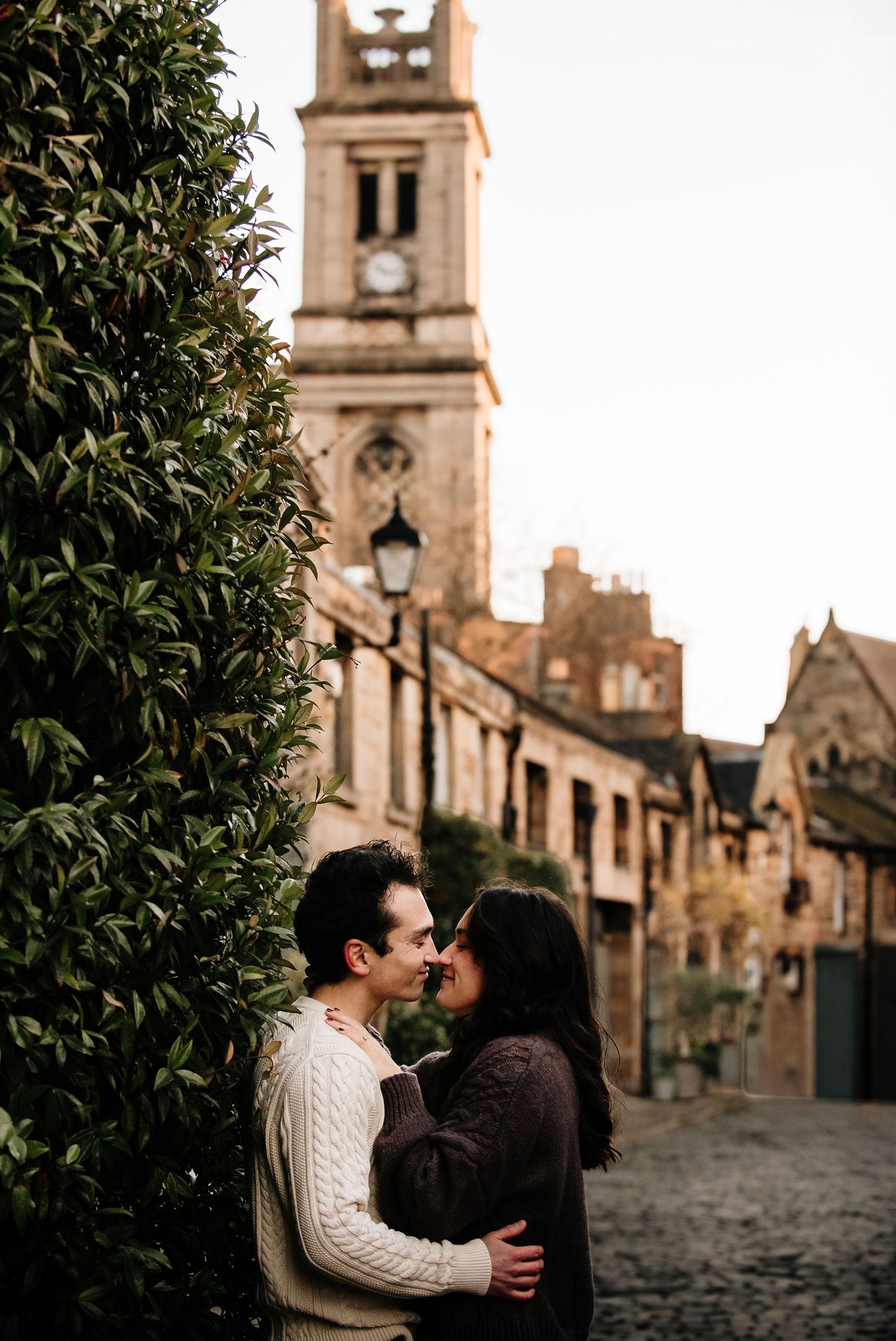 Romantic couple embraces on cobblestone street with historic church architecture in background.