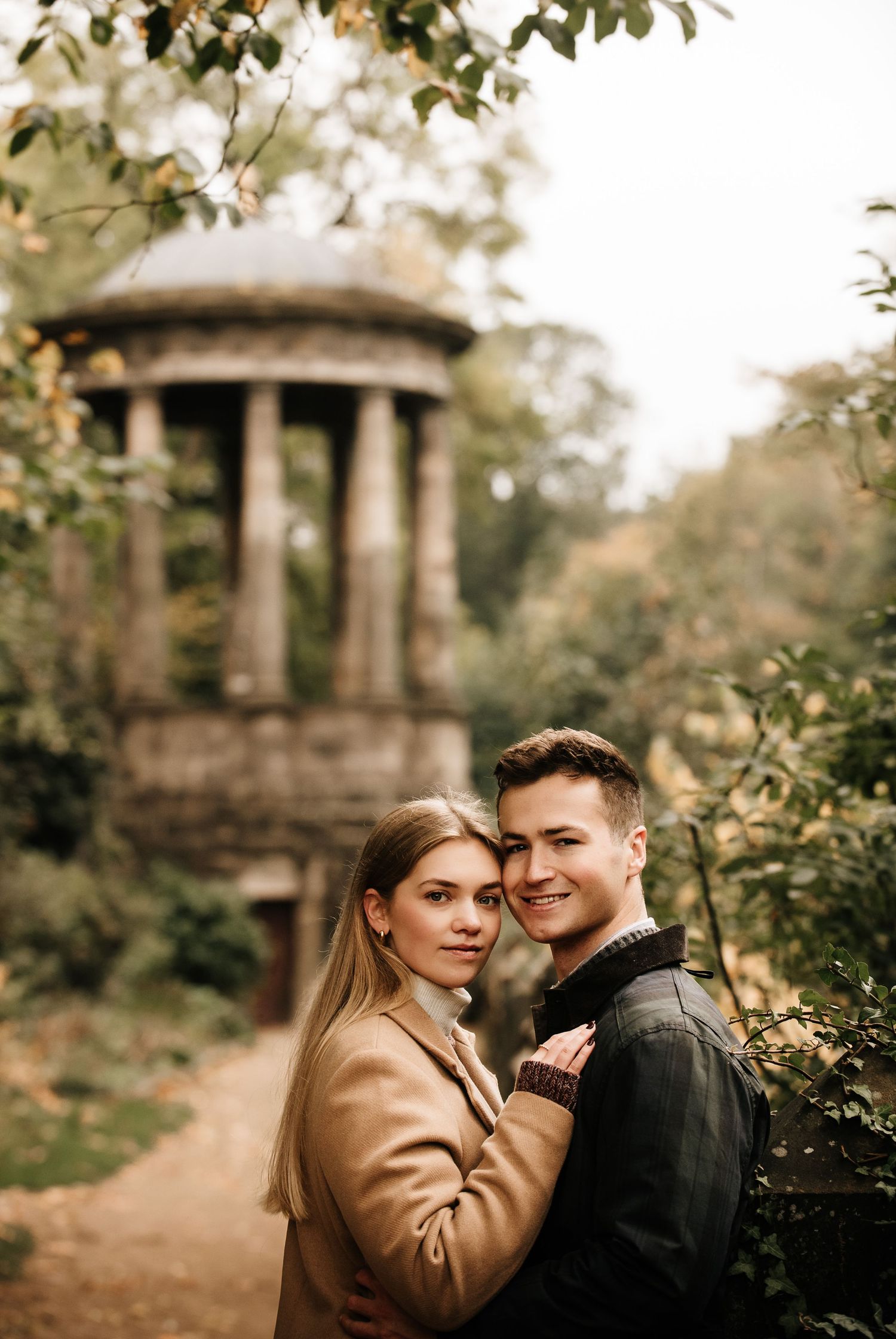 A romantic autumn photoshoot in a garden with a classical stone gazebo in the background.