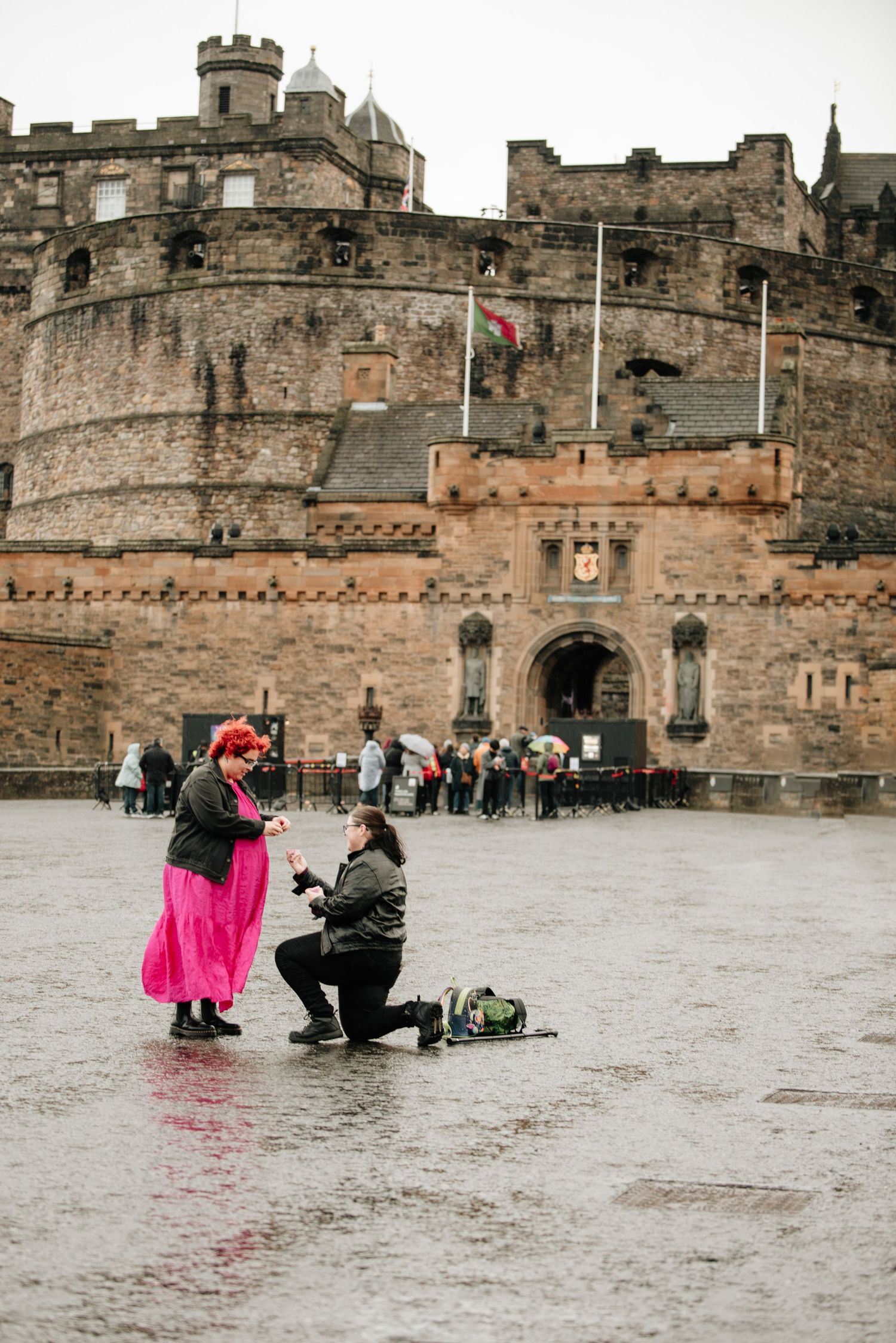 A romantic proposal scene in front of Edinburgh Castle's historic stone walls on a cloudy day.