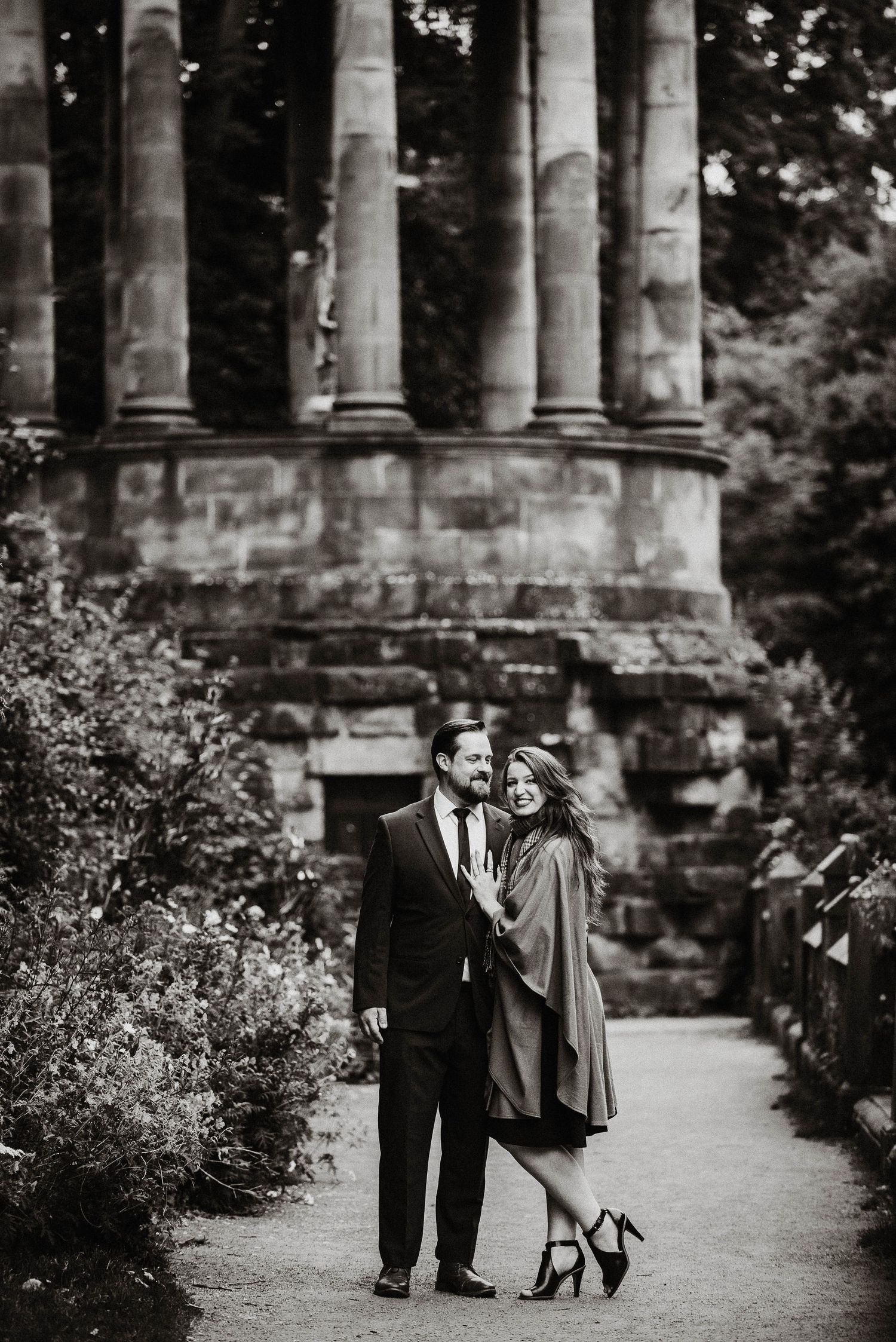 Vintage-style photo of couple embracing among classical stone columns.