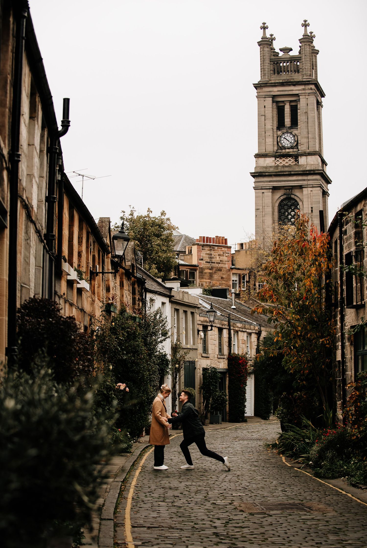 A charming cobblestone street in Edinburgh with historic buildings and a church tower in the background.
