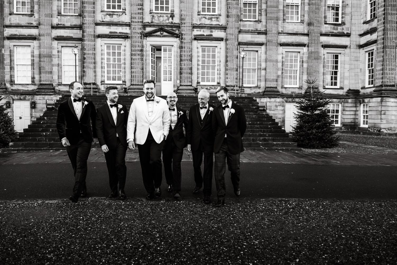 Wedding party silhouettes walking across grand estate grounds at dusk.