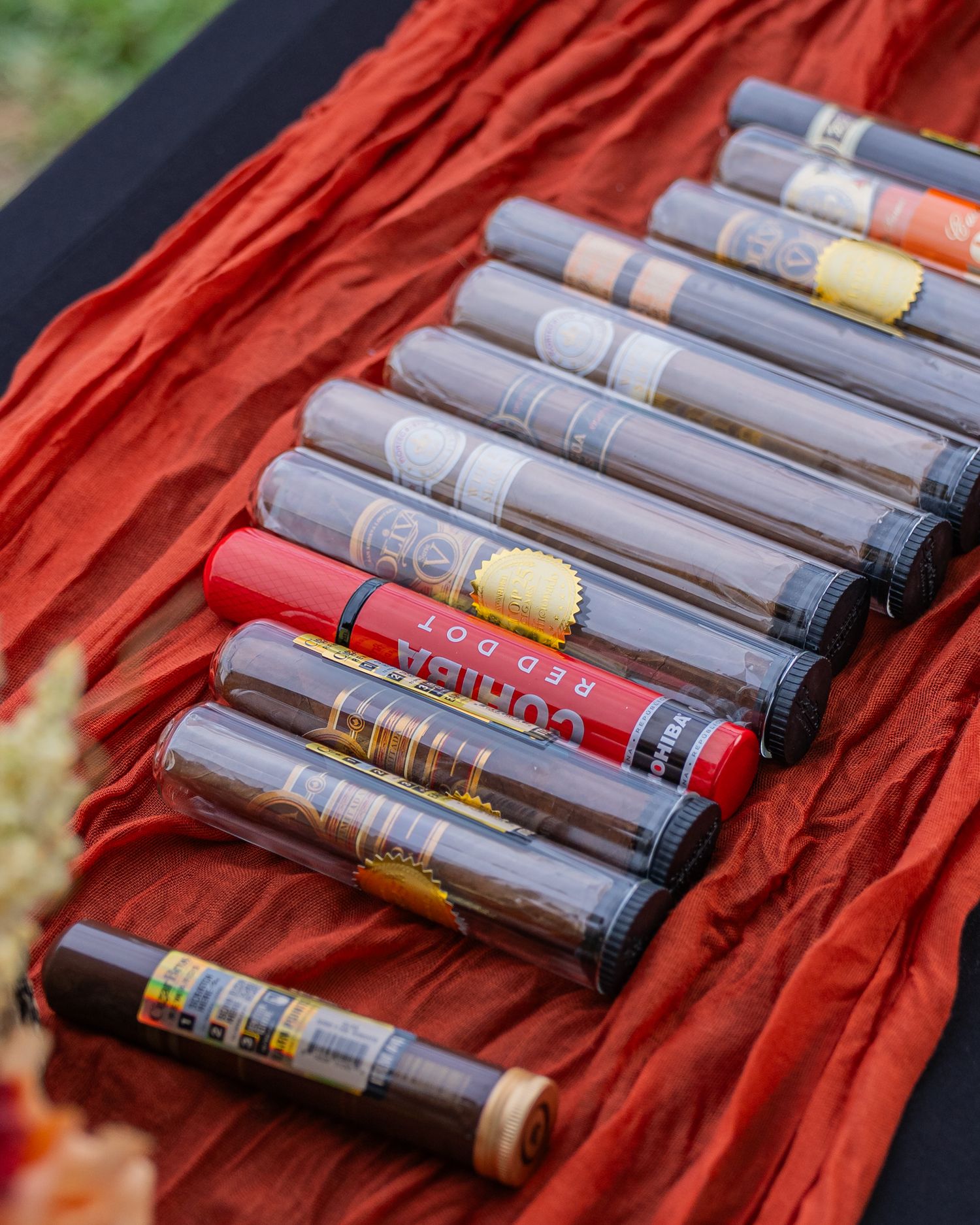 A collection of premium cigars including Cohiba Red Dot displayed on red fabric at an outdoor event.