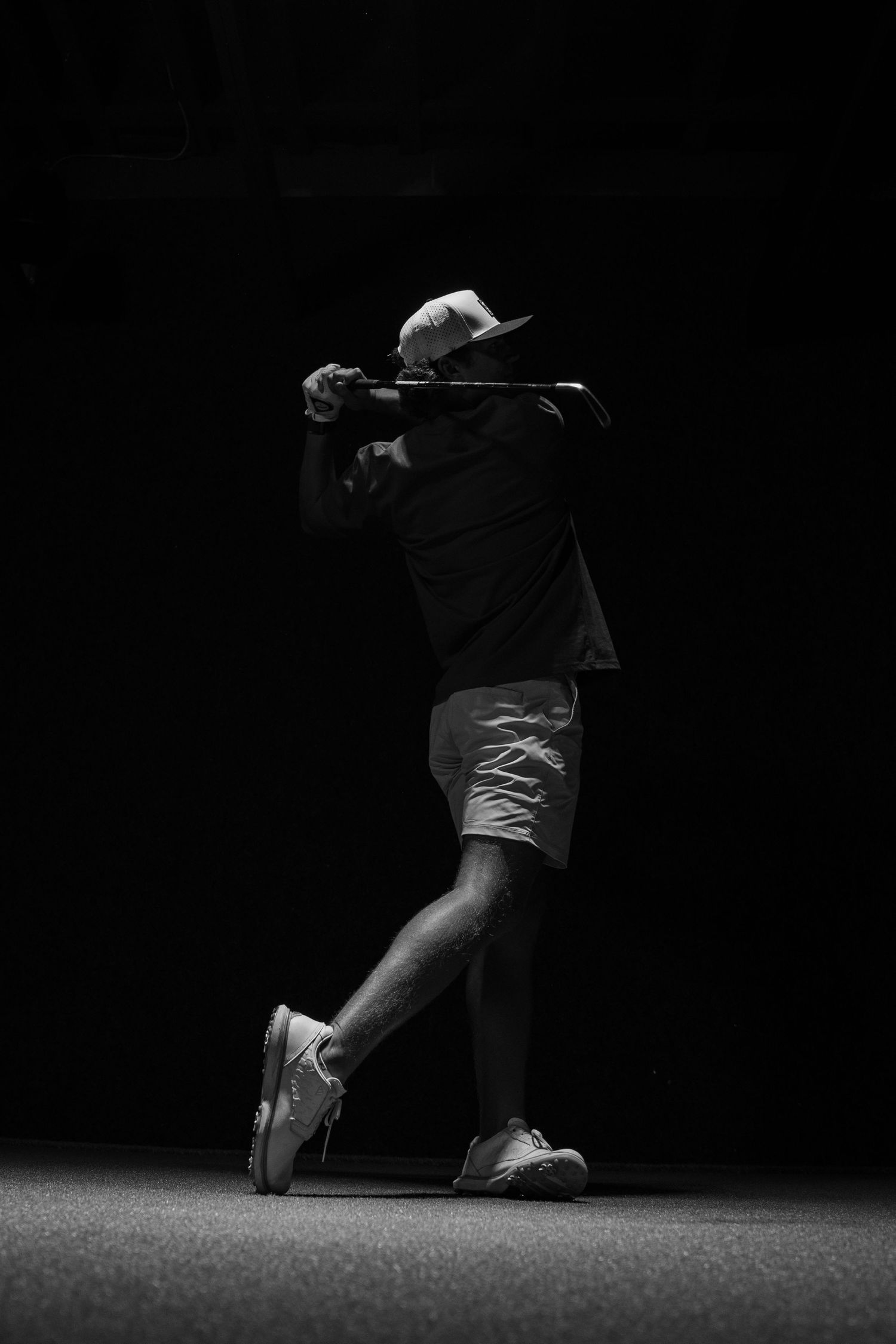 Black and white silhouette of a golfer completing a powerful swing against a dark background.
