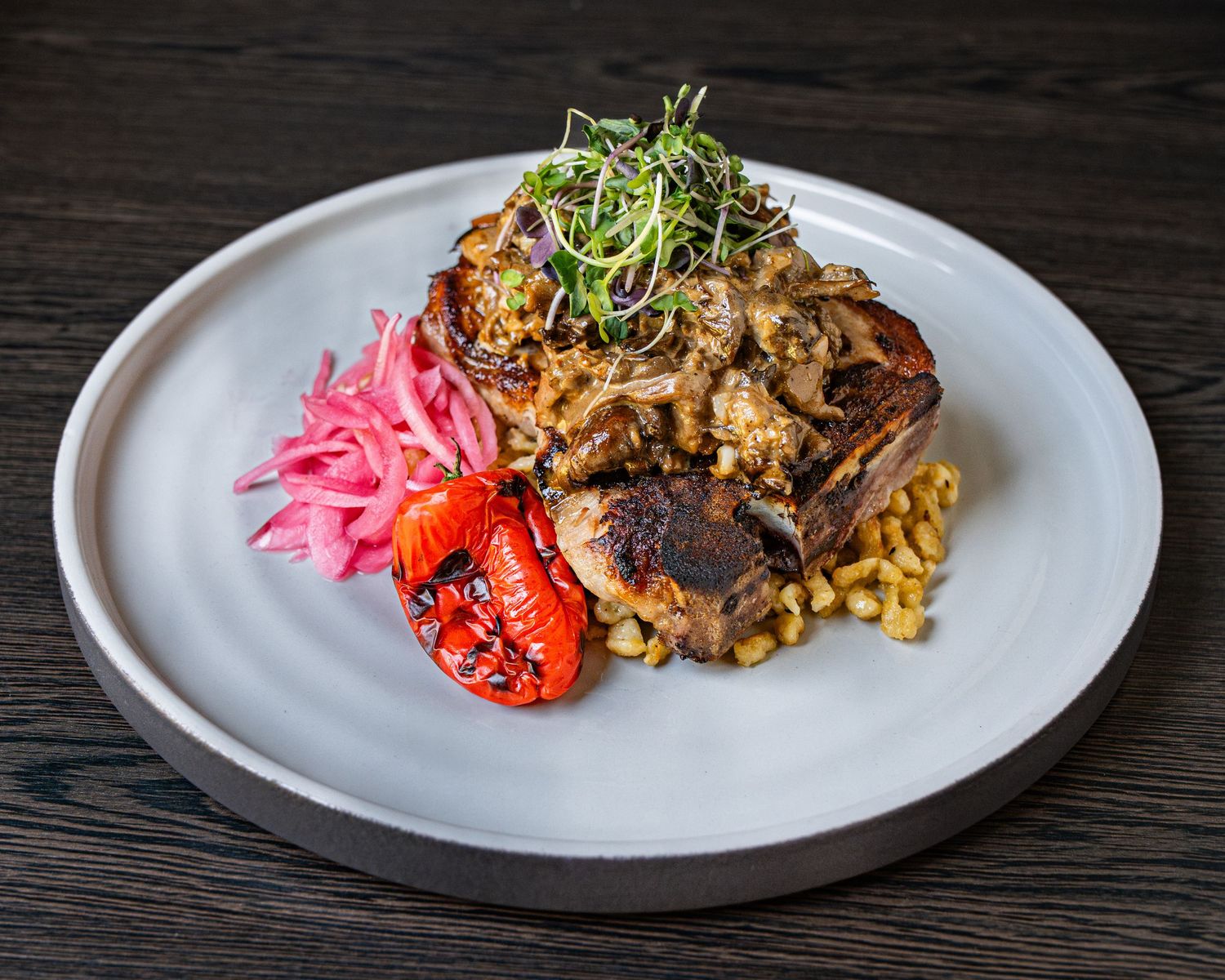 Gourmet plated dish with braised meat, roasted lobster, corn, pickled onions, and microgreens on a white ceramic plate.