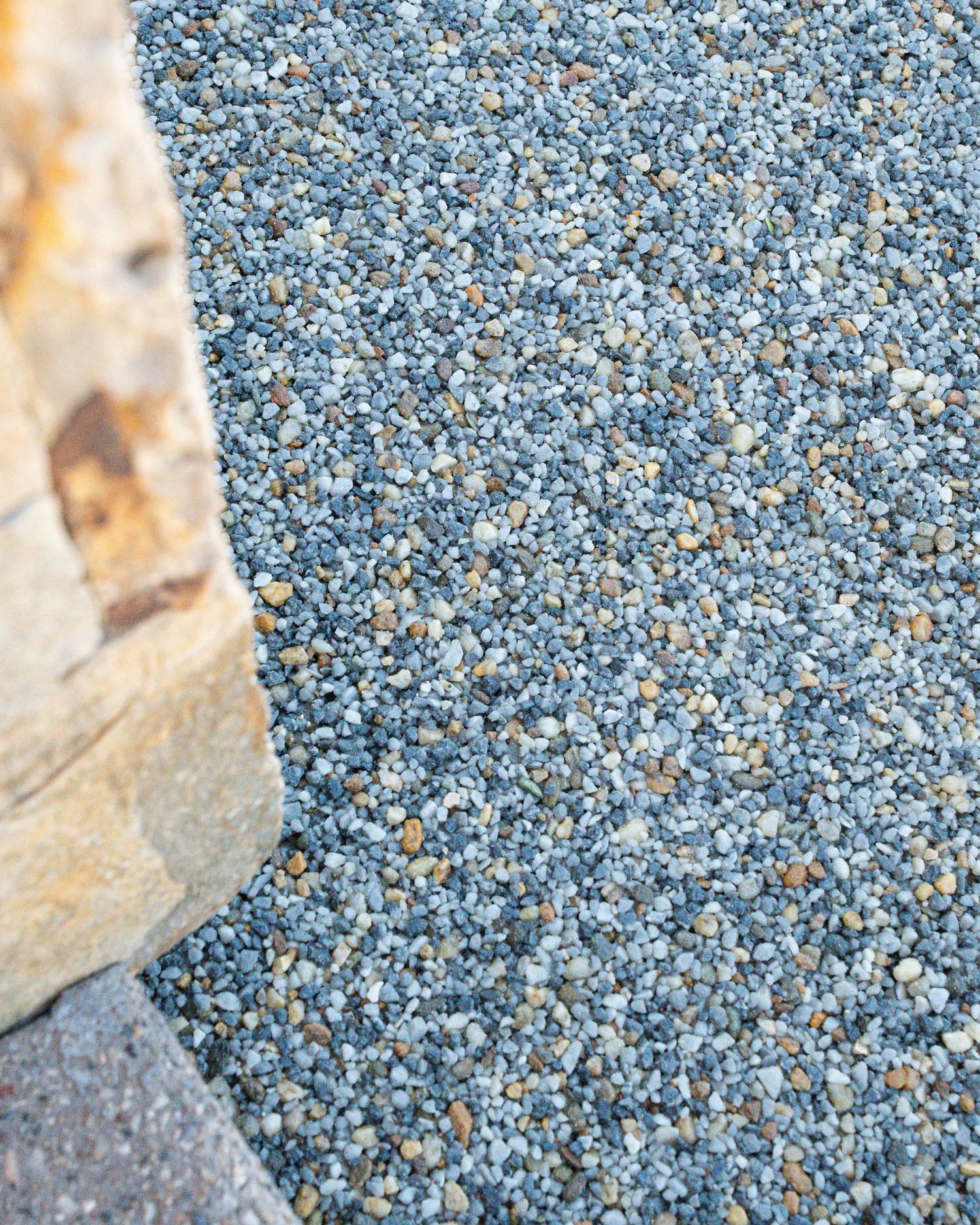 Close-up of blue-gray pea gravel ground cover next to a natural stone edge in an outdoor landscape.