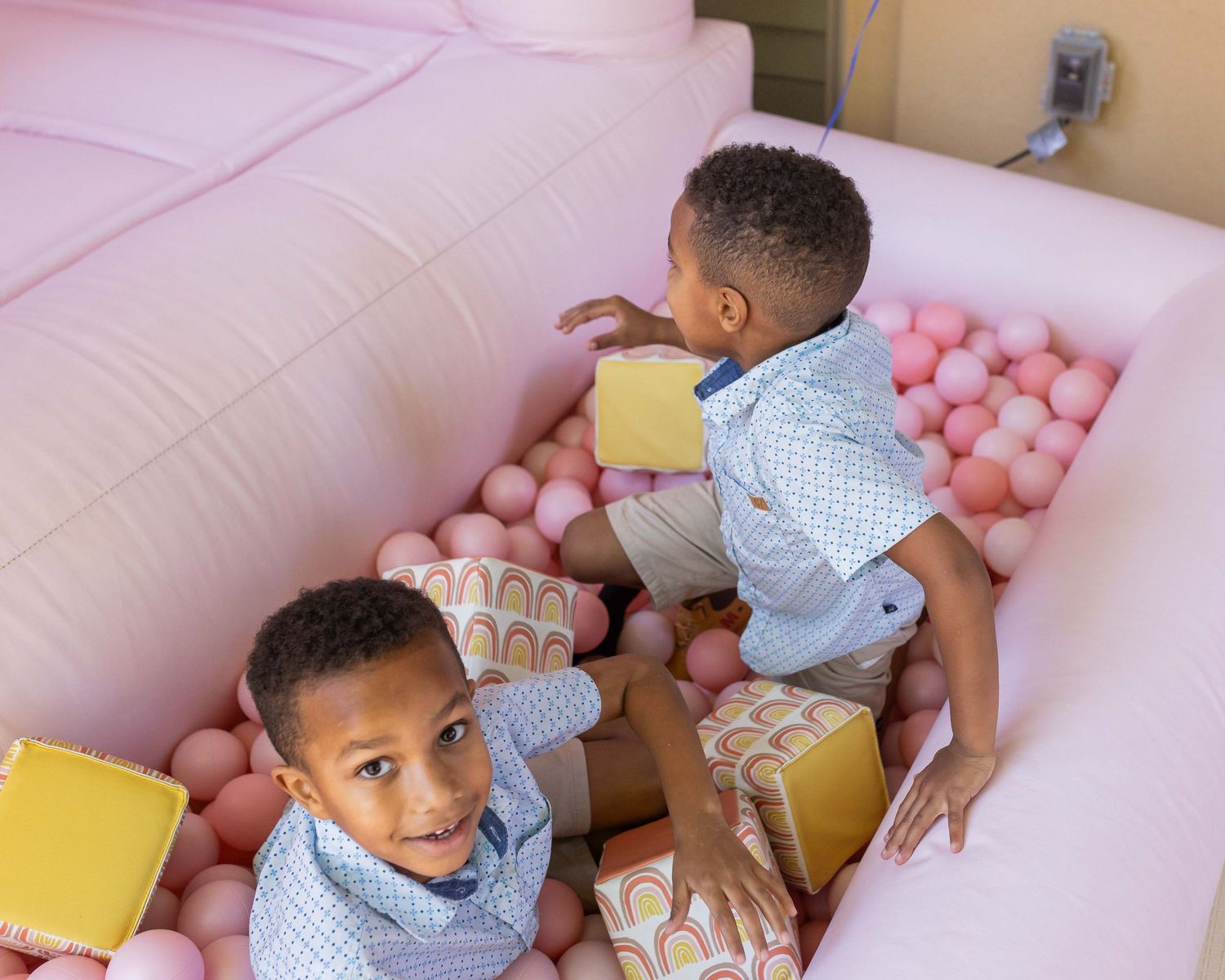 Children playing with pink balloons and alphabet blocks in a cozy indoor setting.
