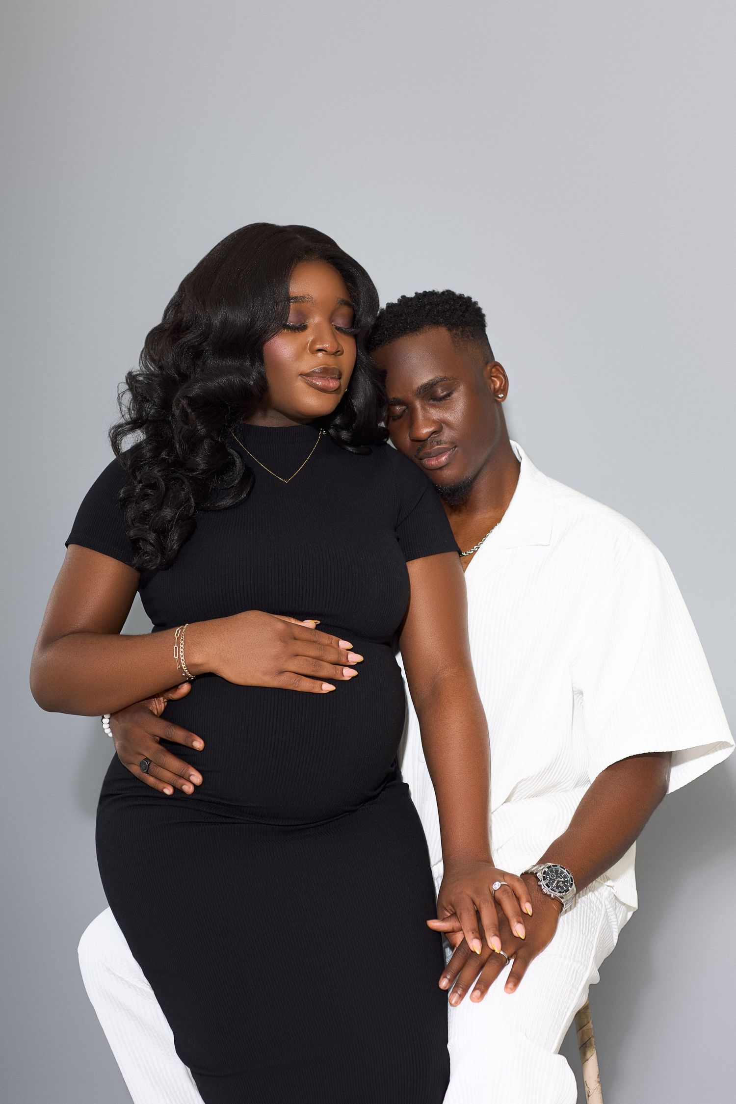 A couple poses intimately in black and white outfits against a light background.