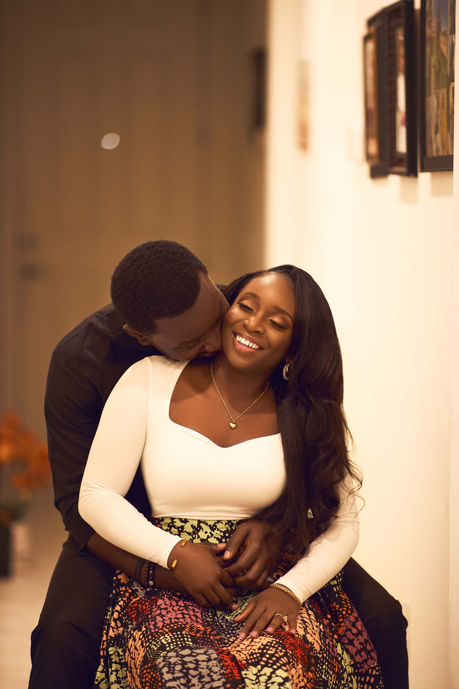 A couple sharing playful and romantic moments in an indoor photoshoot with warm lighting.