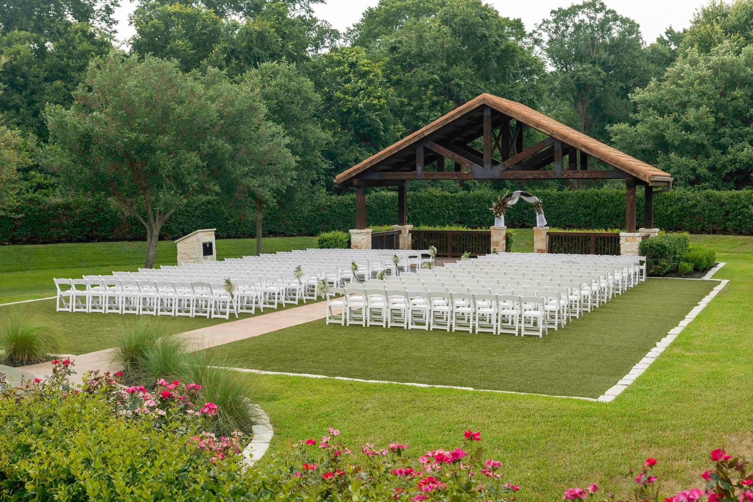 Outdoor wedding ceremony setup with white chairs and floral arrangements on a lawn.