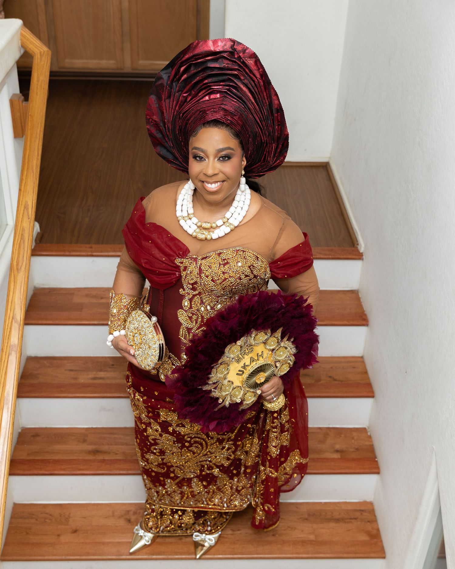 Traditional bridesmaids in burgundy and gold attire gather on wooden staircase.