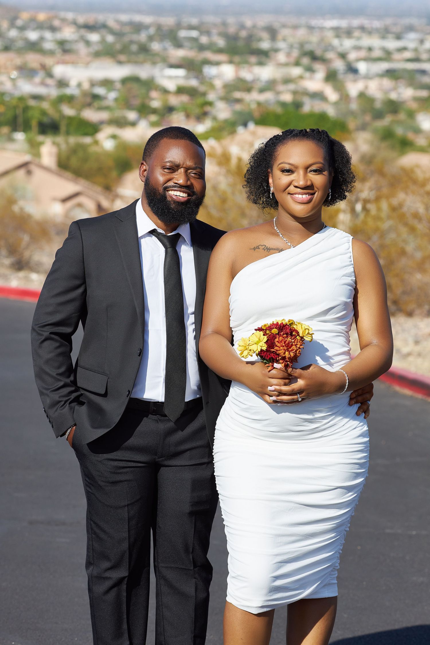 Couple poses for outdoor wedding photos with cityscape backdrop.