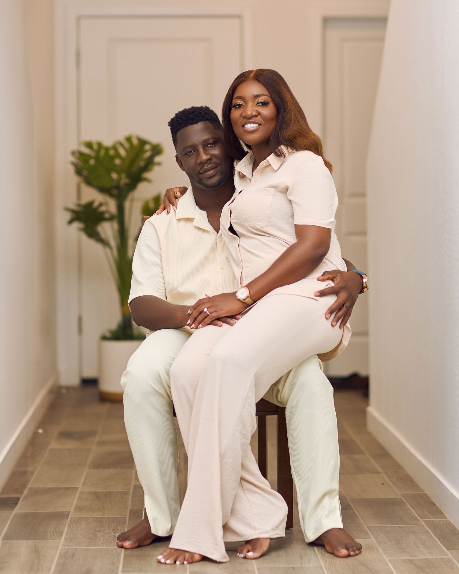 Couple wearing all white sits together in bright hallway for engagement photos.
