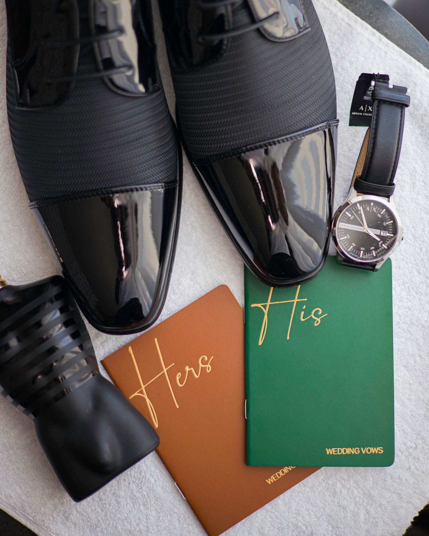 A row of wedding vows books in brown and green colors arranged next to black formal shoes on a white surface.