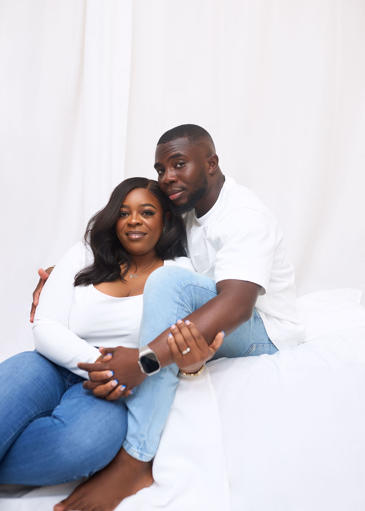 A couple in casual attire sharing intimate moments on a white couch in a series of romantic poses.