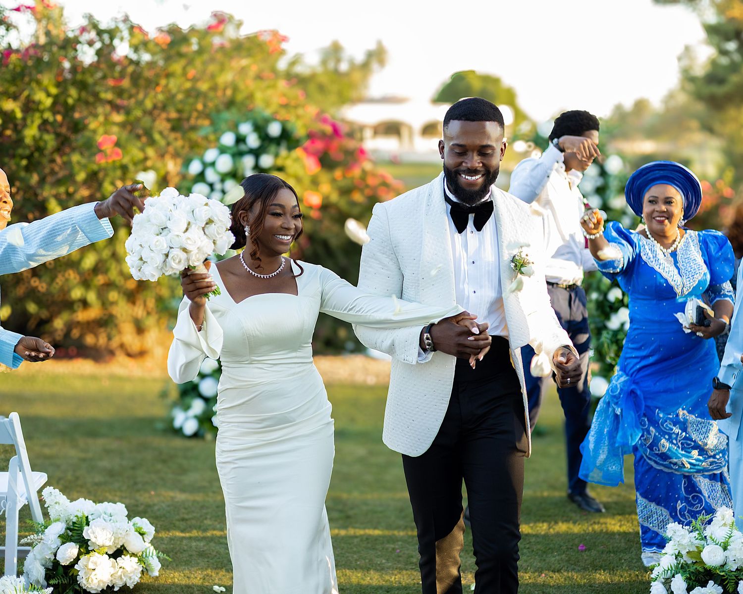 Joyful wedding celebration outdoors with white floral decorations and vibrant autumn foliage in the background.