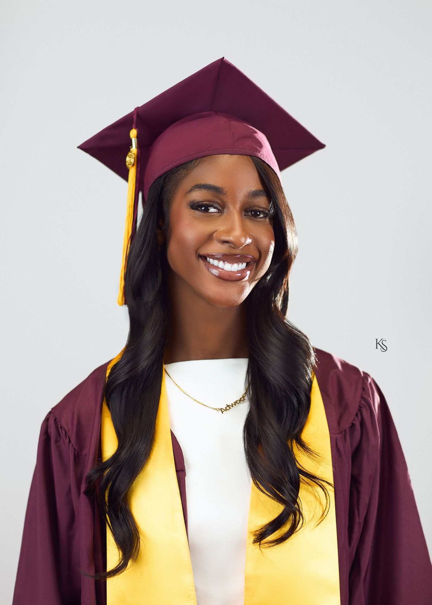 Professional graduation photoshoot featuring maroon cap and gown with yellow accents against white background.