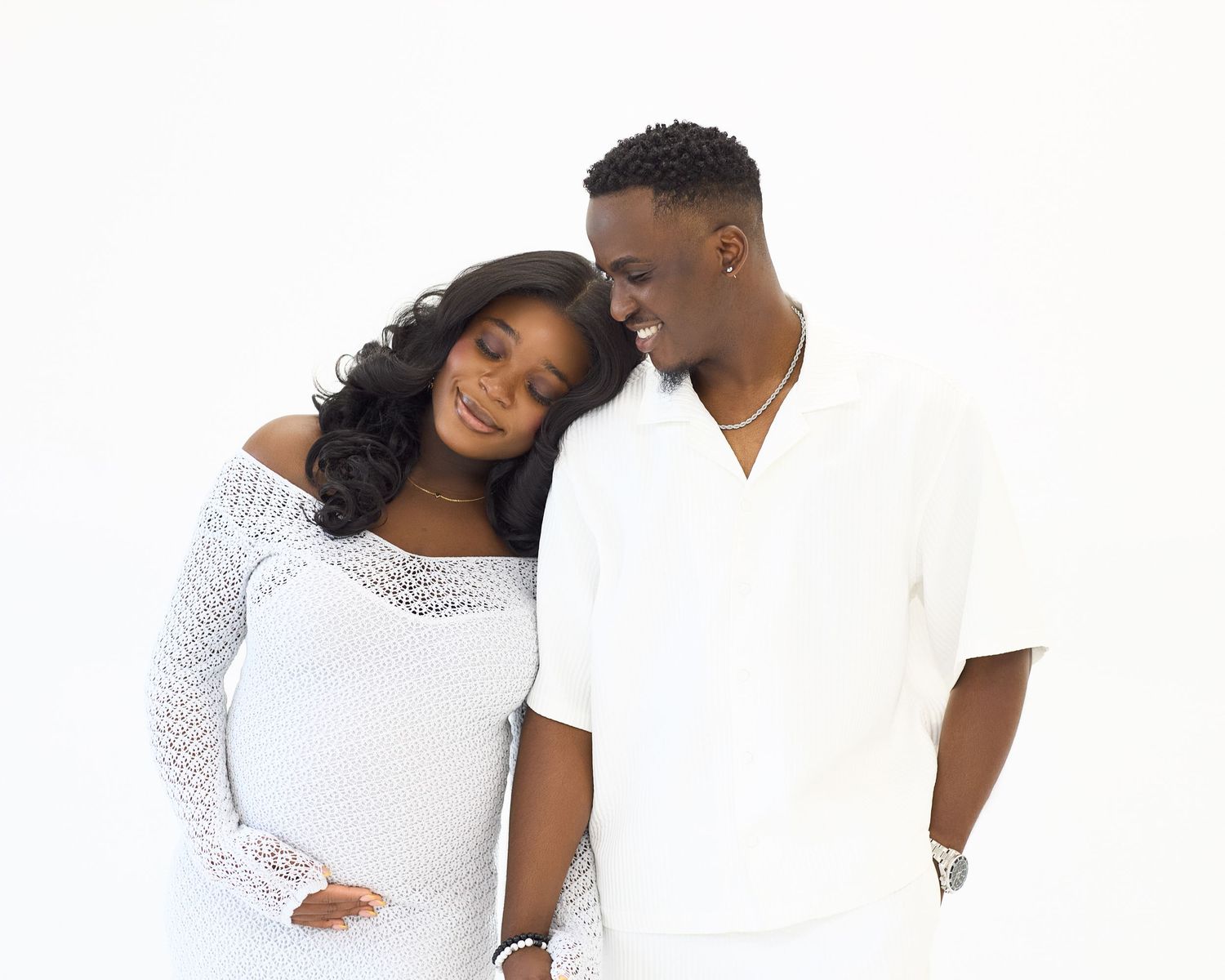 Couple embraces in all-white outfits during studio photoshoot.
