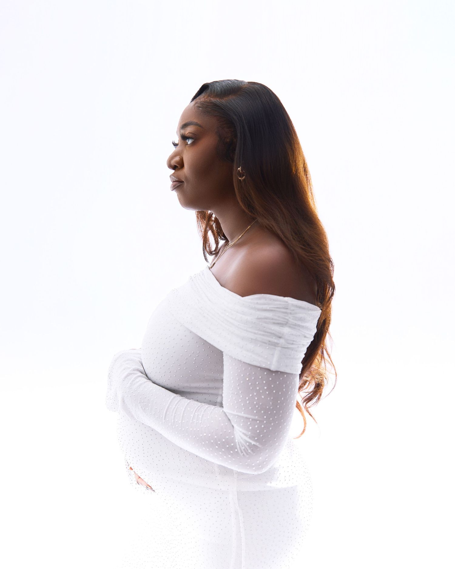 Side profile maternity portrait in white off-shoulder gown with dramatic lighting.