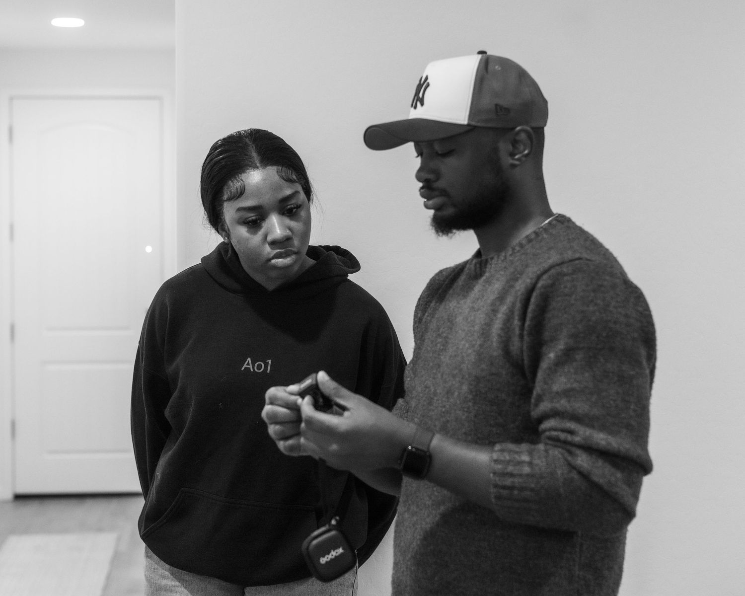 A couple in dark clothing interacts casually in black and white photos.