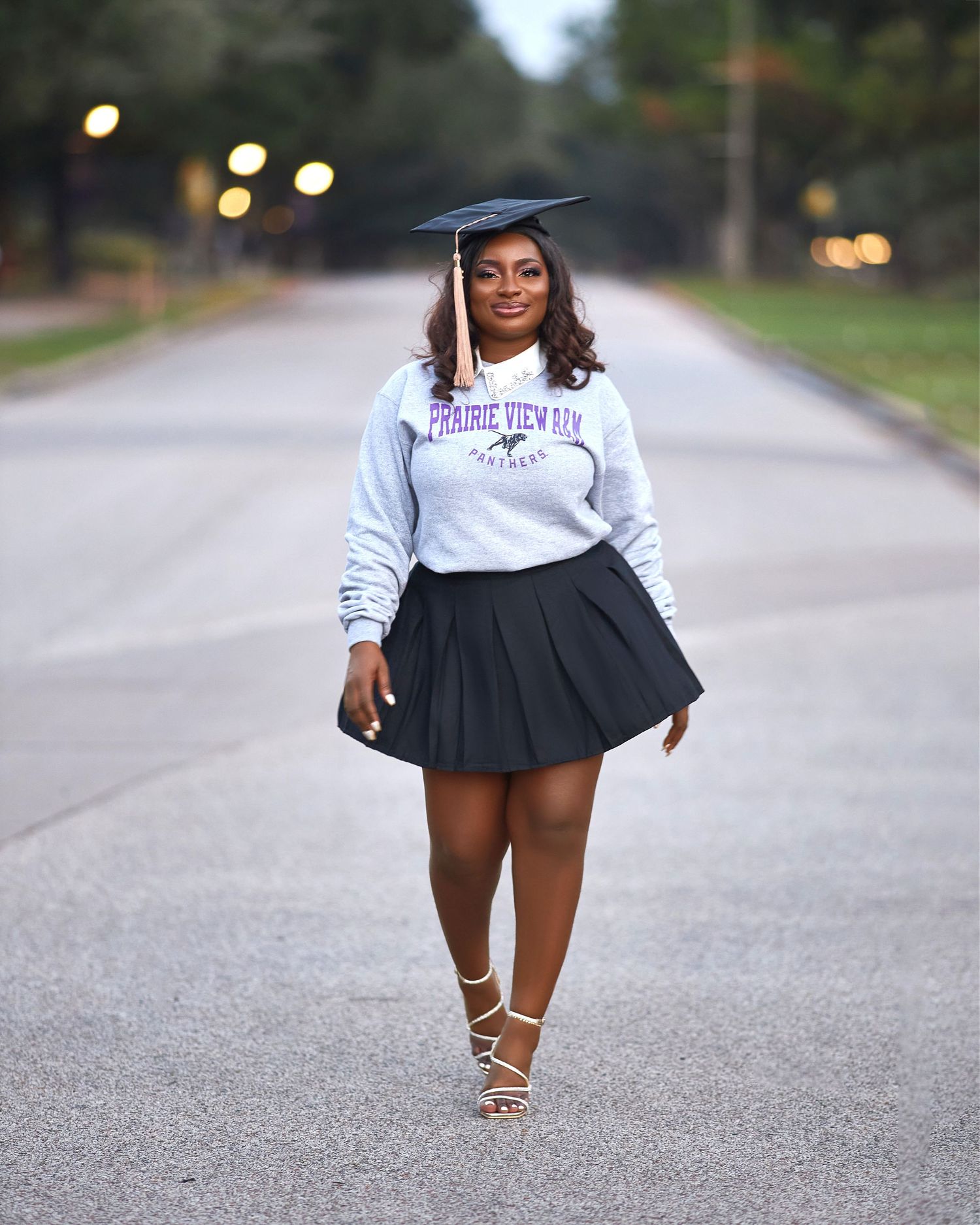 Graduate in white sweater and navy skirt poses on empty road for outdoor photo session.