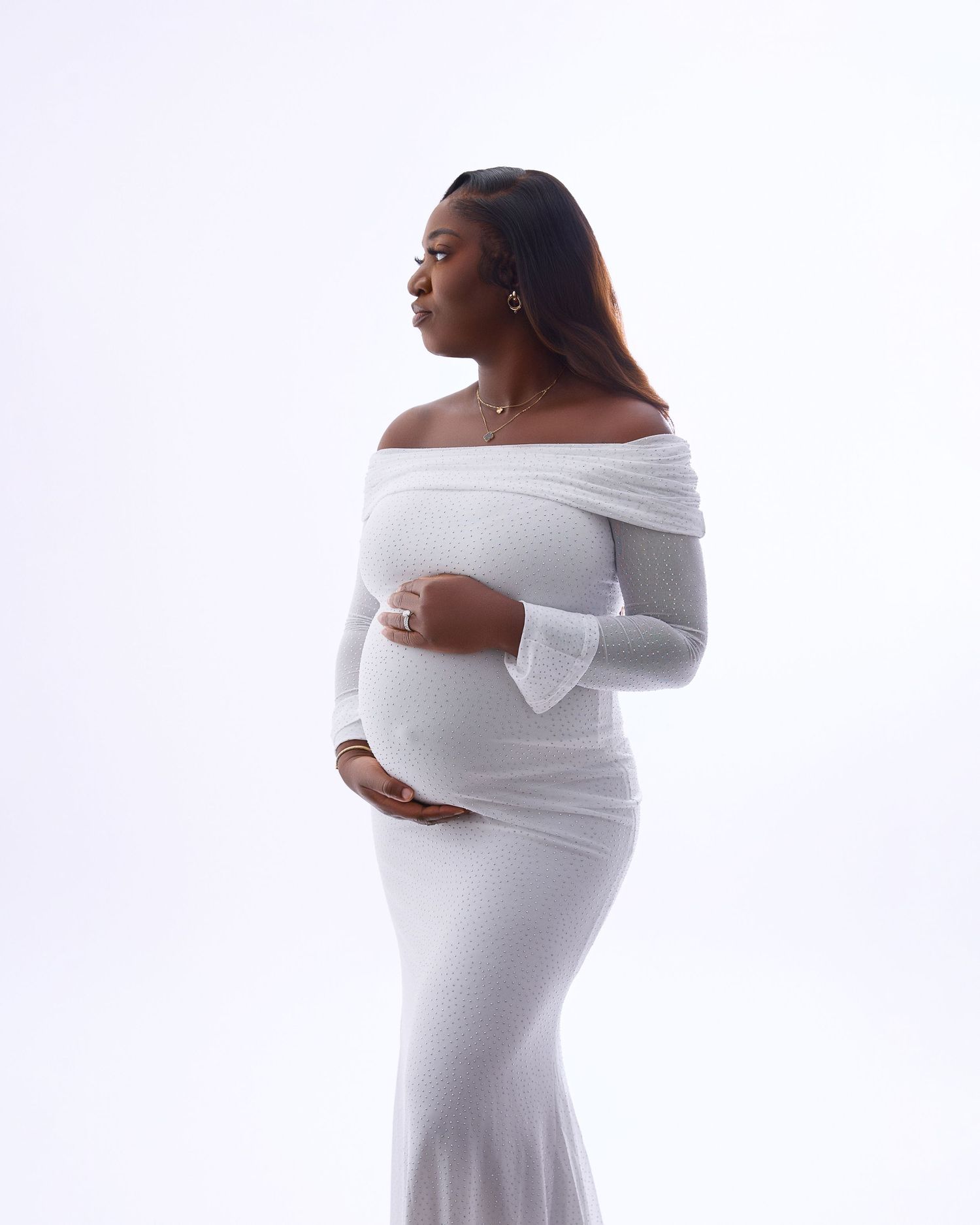Elegant maternity portrait in form-fitting white off-shoulder gown with bell sleeves.