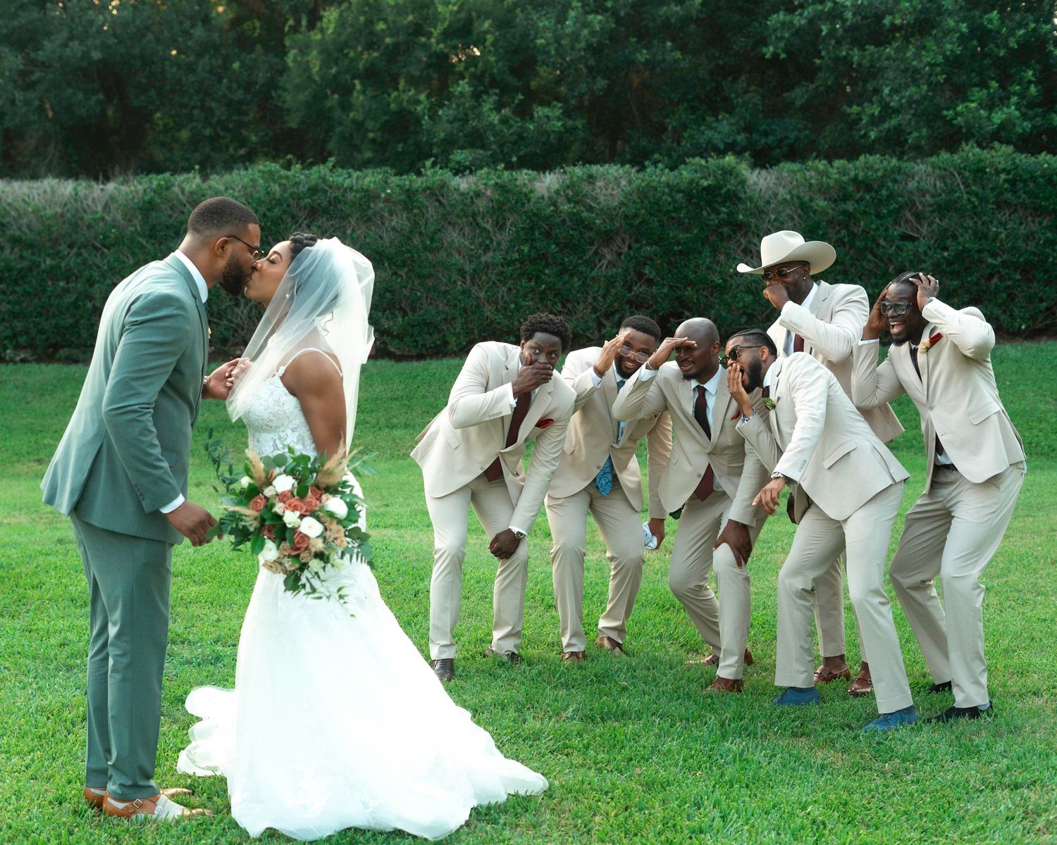 Wedding party performs choreographed dance moves on green lawn.