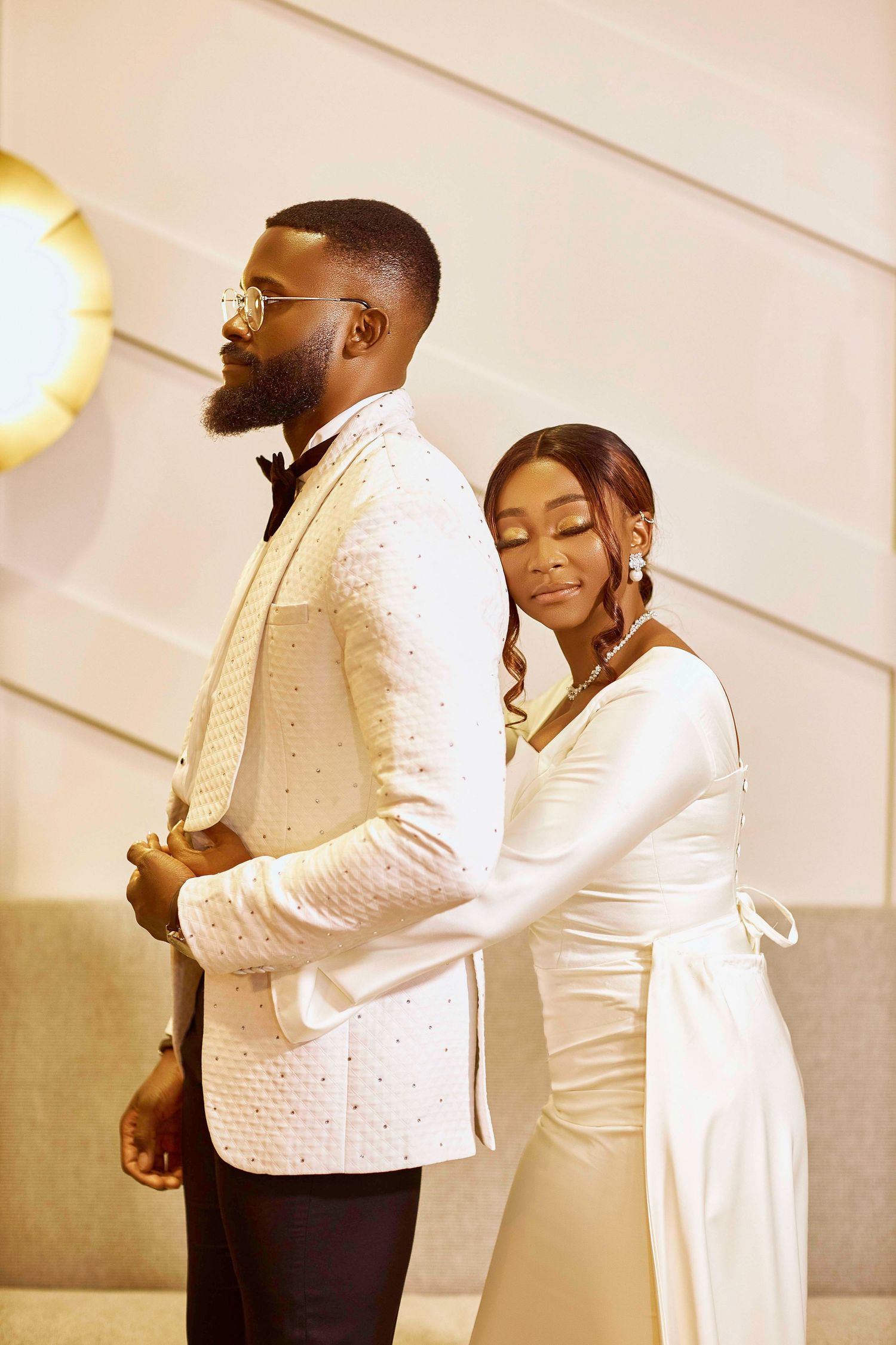 An elegant couple in white formal wear shares tender moments indoors.