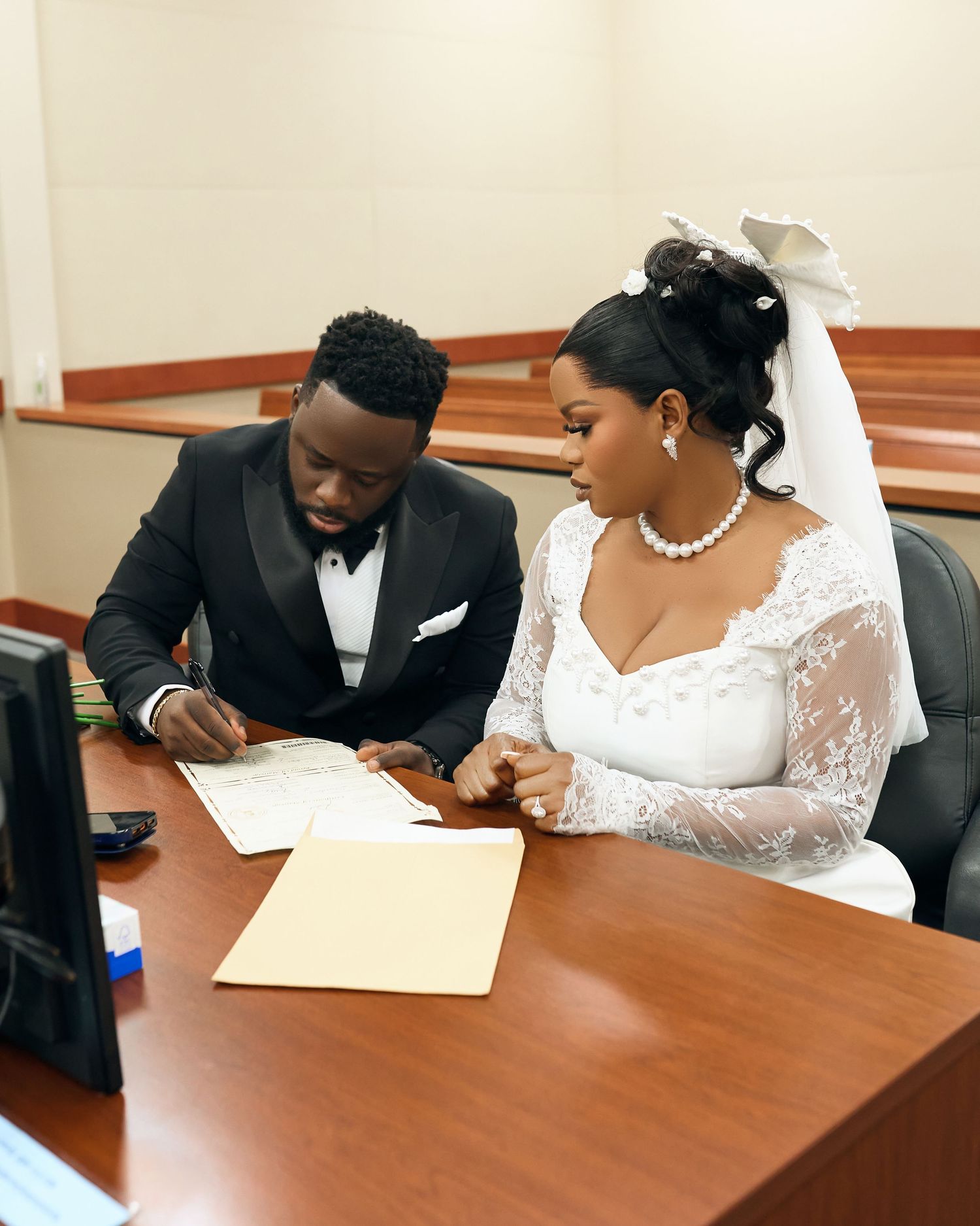 A couple signs marriage documents at a wooden table indoors.