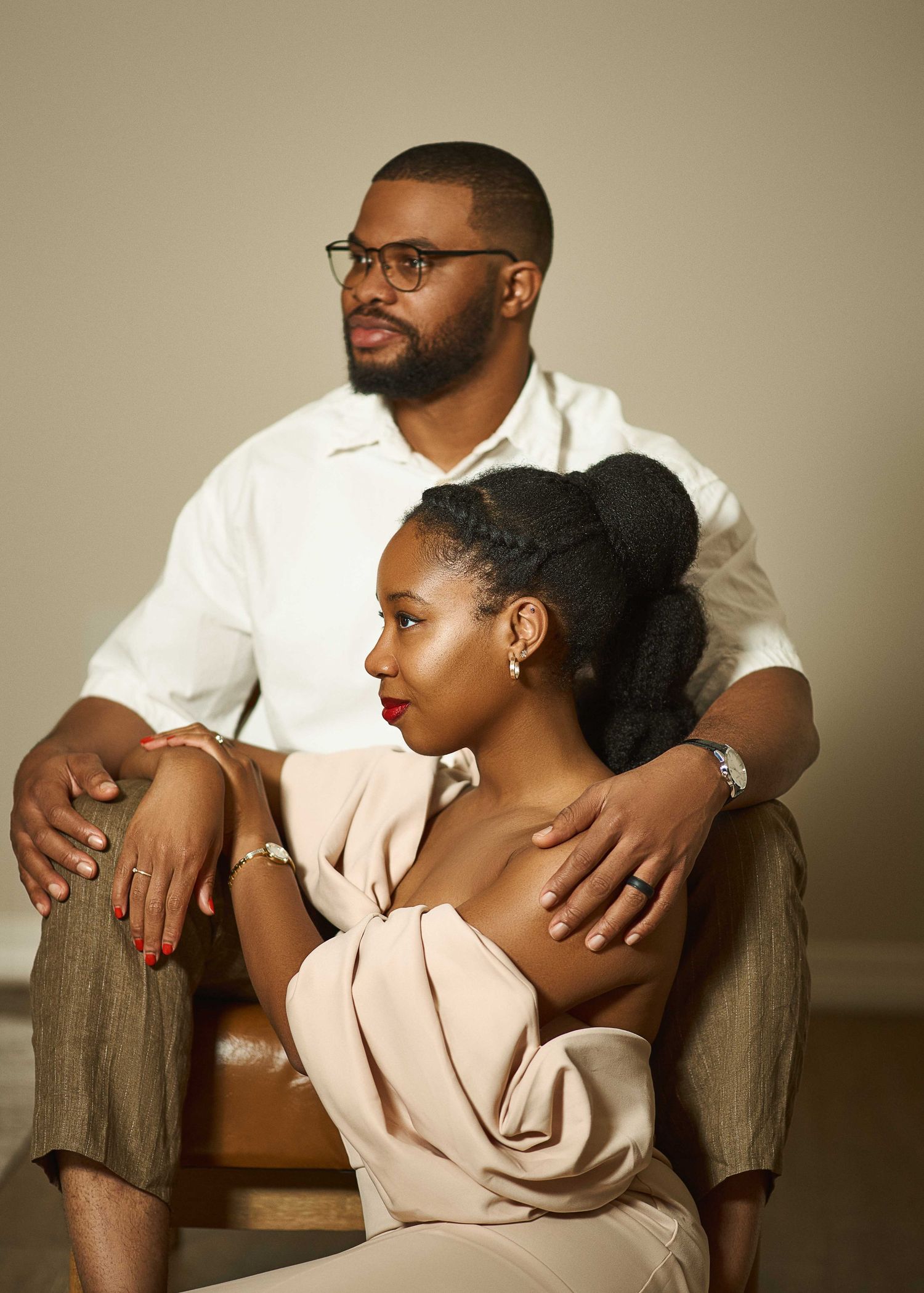 Couple poses intimately on brown couch during indoor photoshoot.