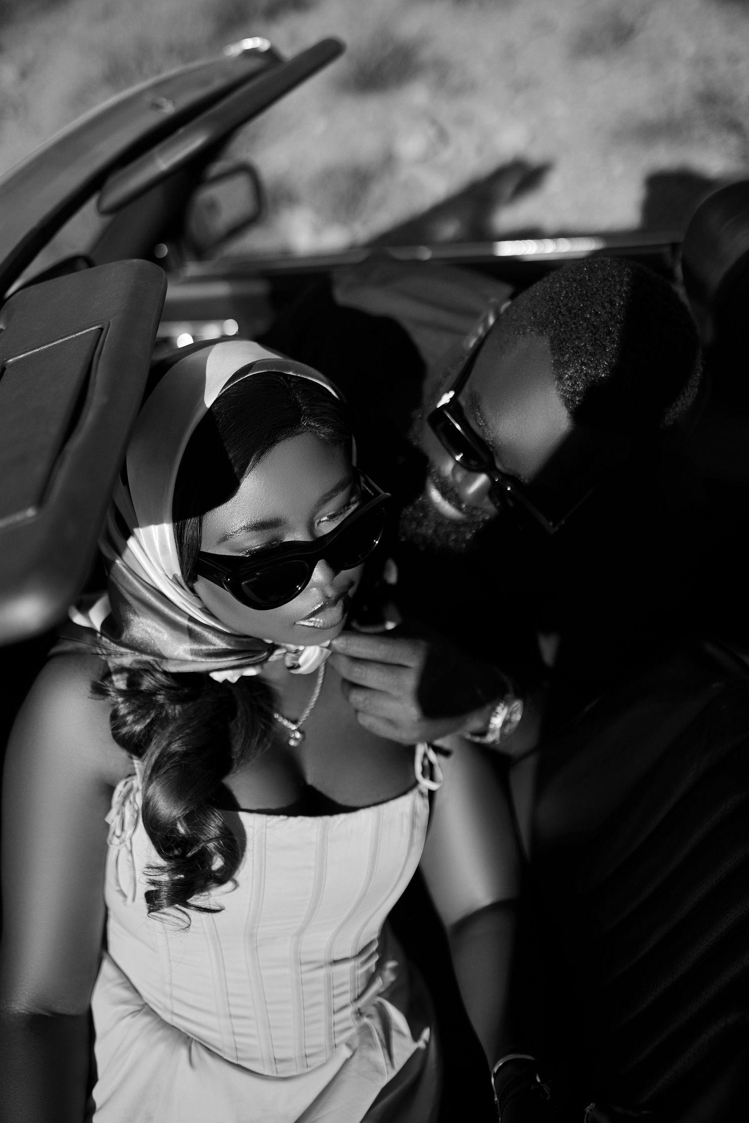 Black and white photo of couple in convertible car wearing stylish sunglasses.
