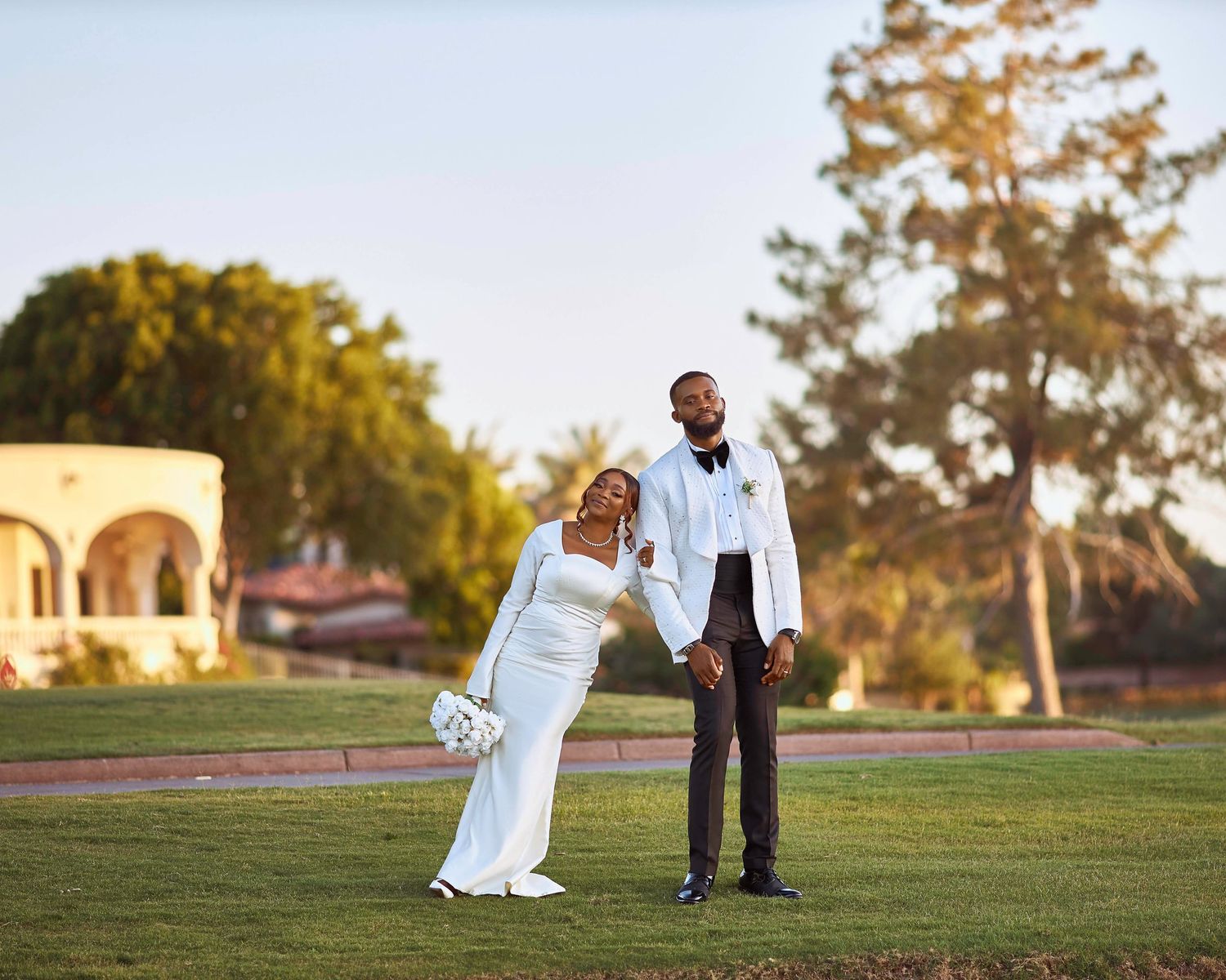 A wedding couple poses on a grassy hill during golden hour.