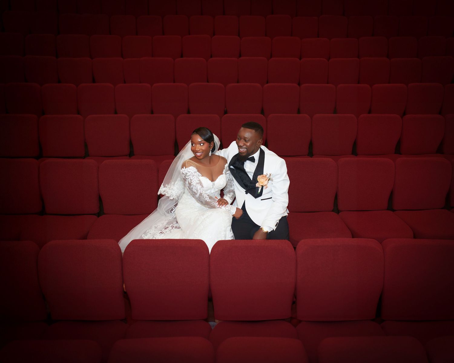 Couple sits together in empty red theater seats during romantic photoshoot.