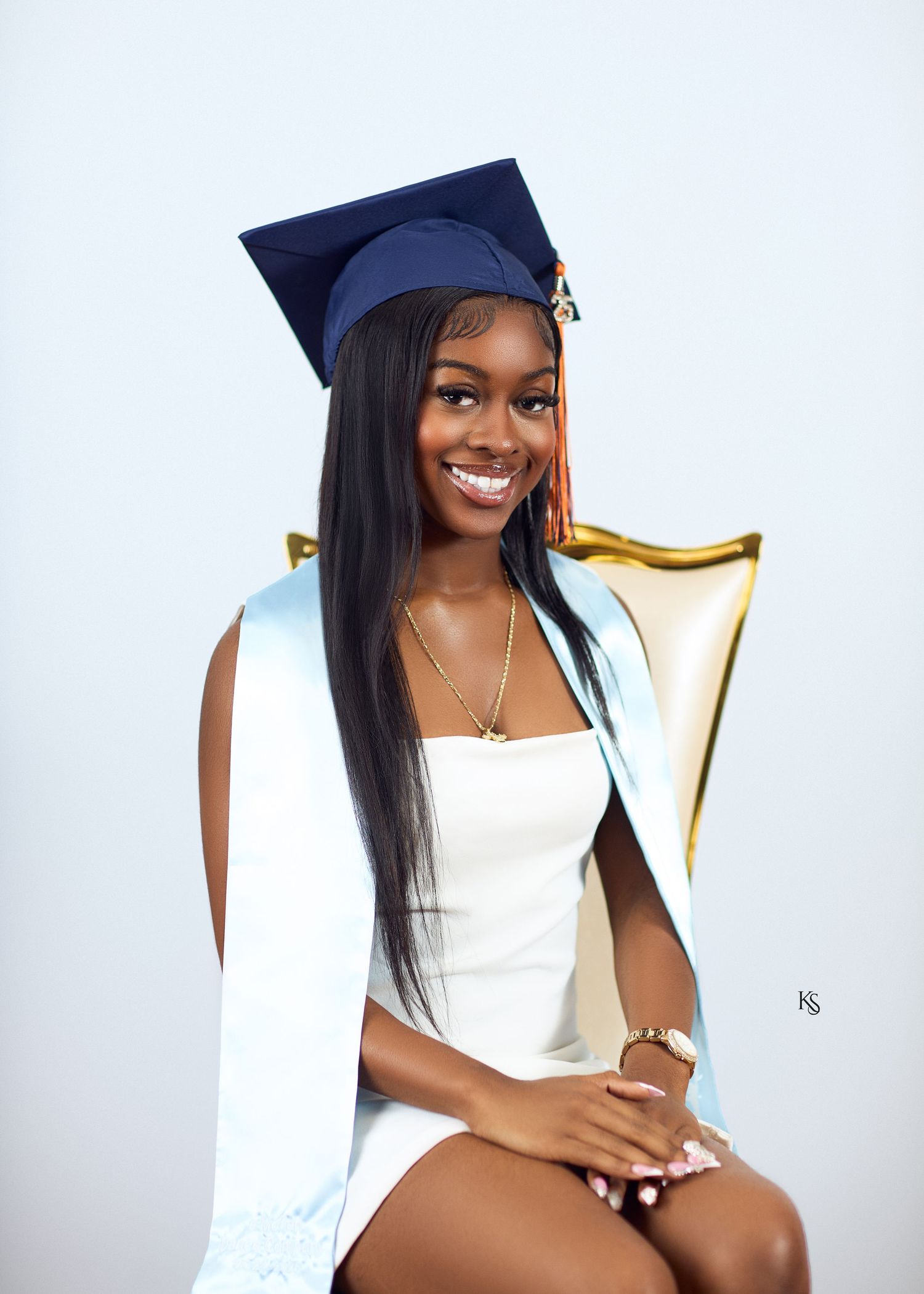 Graduate in navy cap and white dress poses elegantly against white backdrop for professional photos.