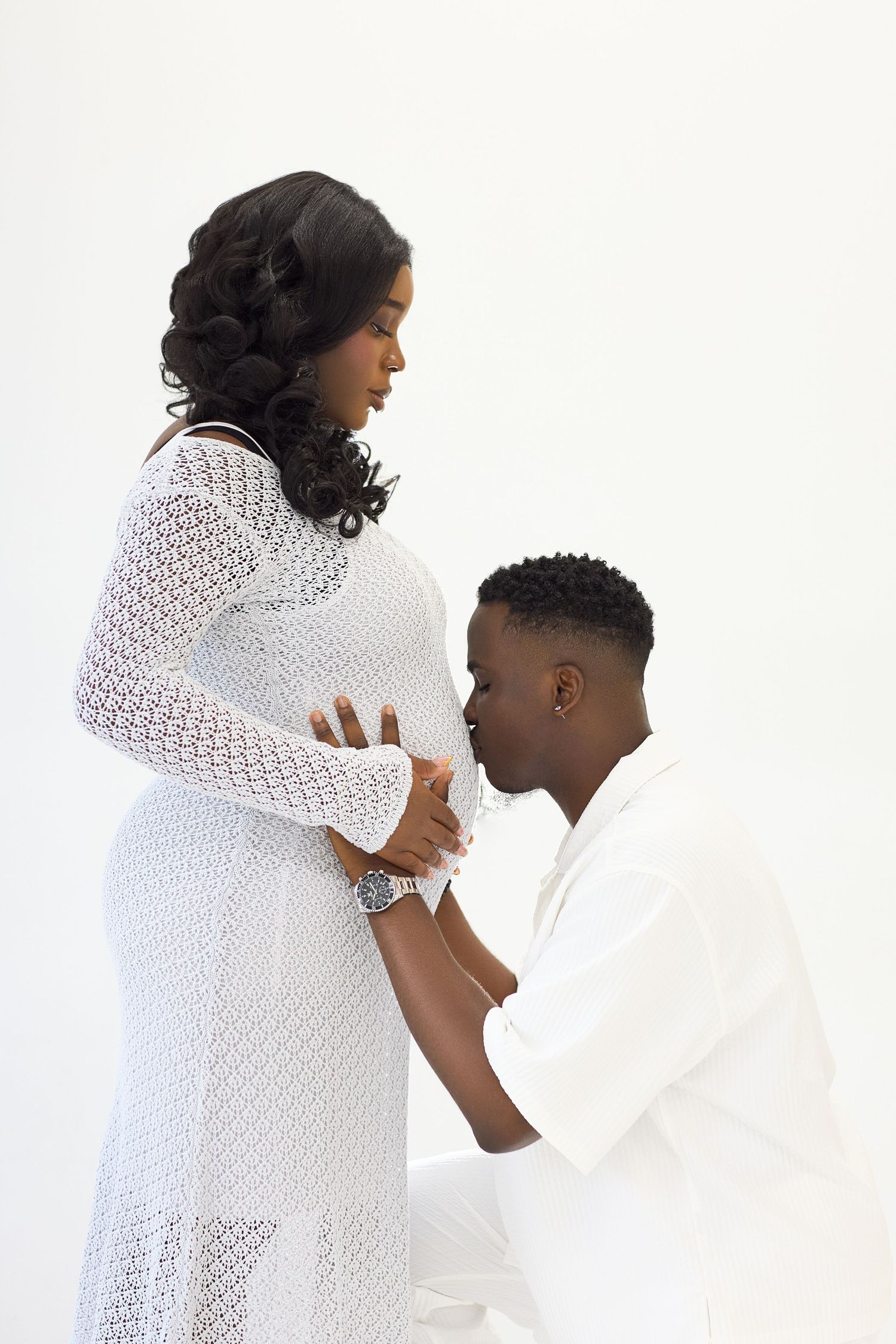 Romantic couple in white outfits poses against bright studio backdrop.
