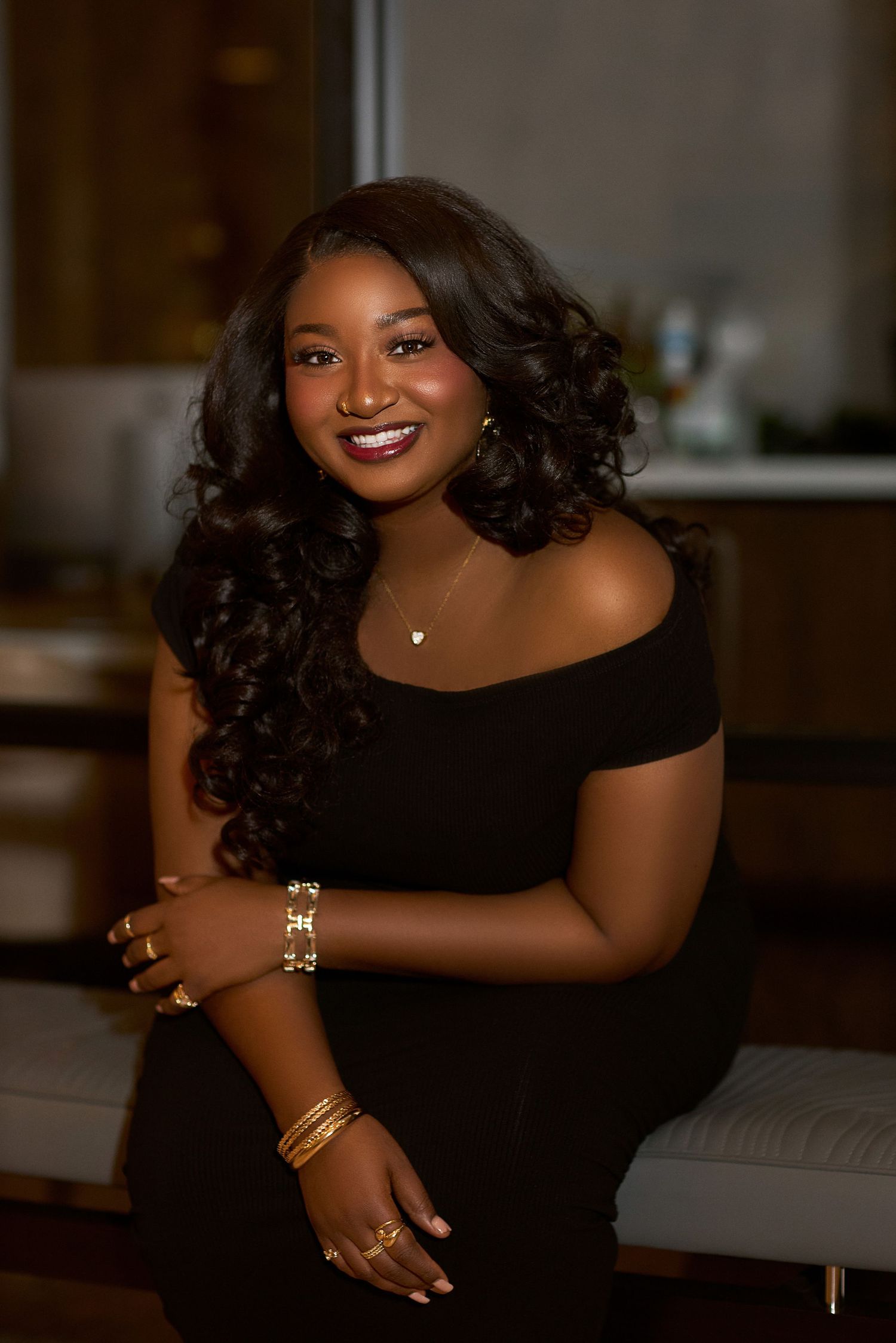 Studio portraits in black dress with curled hair and gold accessories against dark background.