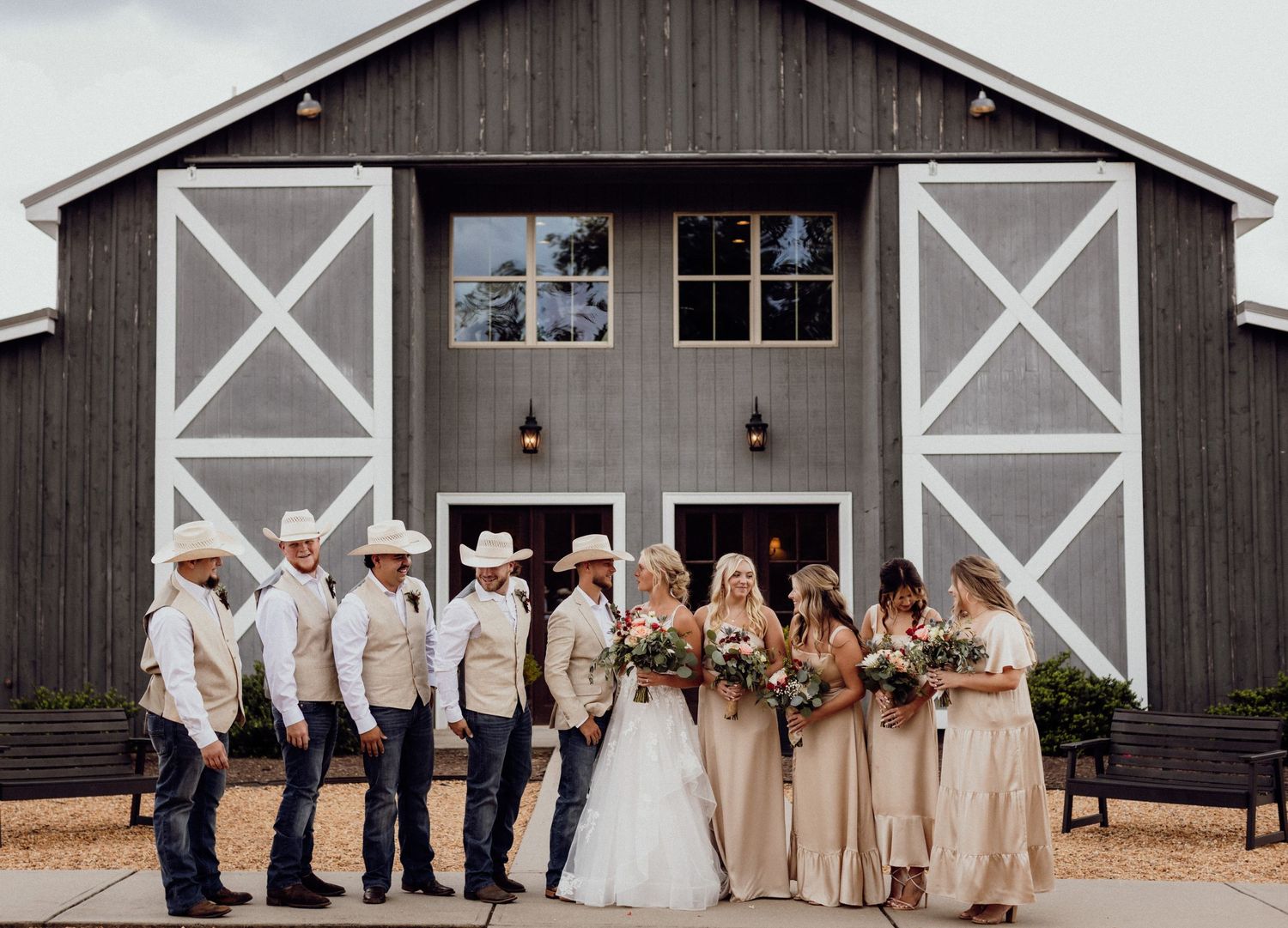 Wedding party lineup in neutral tones standing in front of a rustic barn venue.