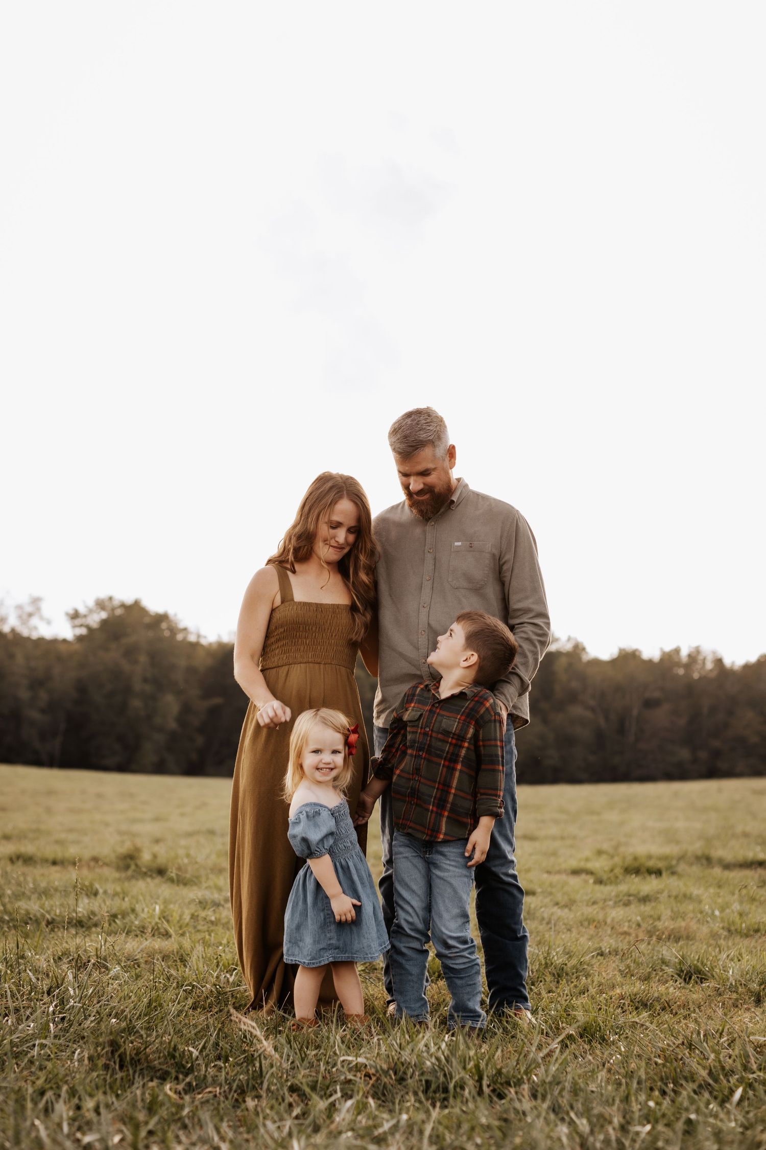 Family in casual attire poses together in a sunlit grassy field at sunset.