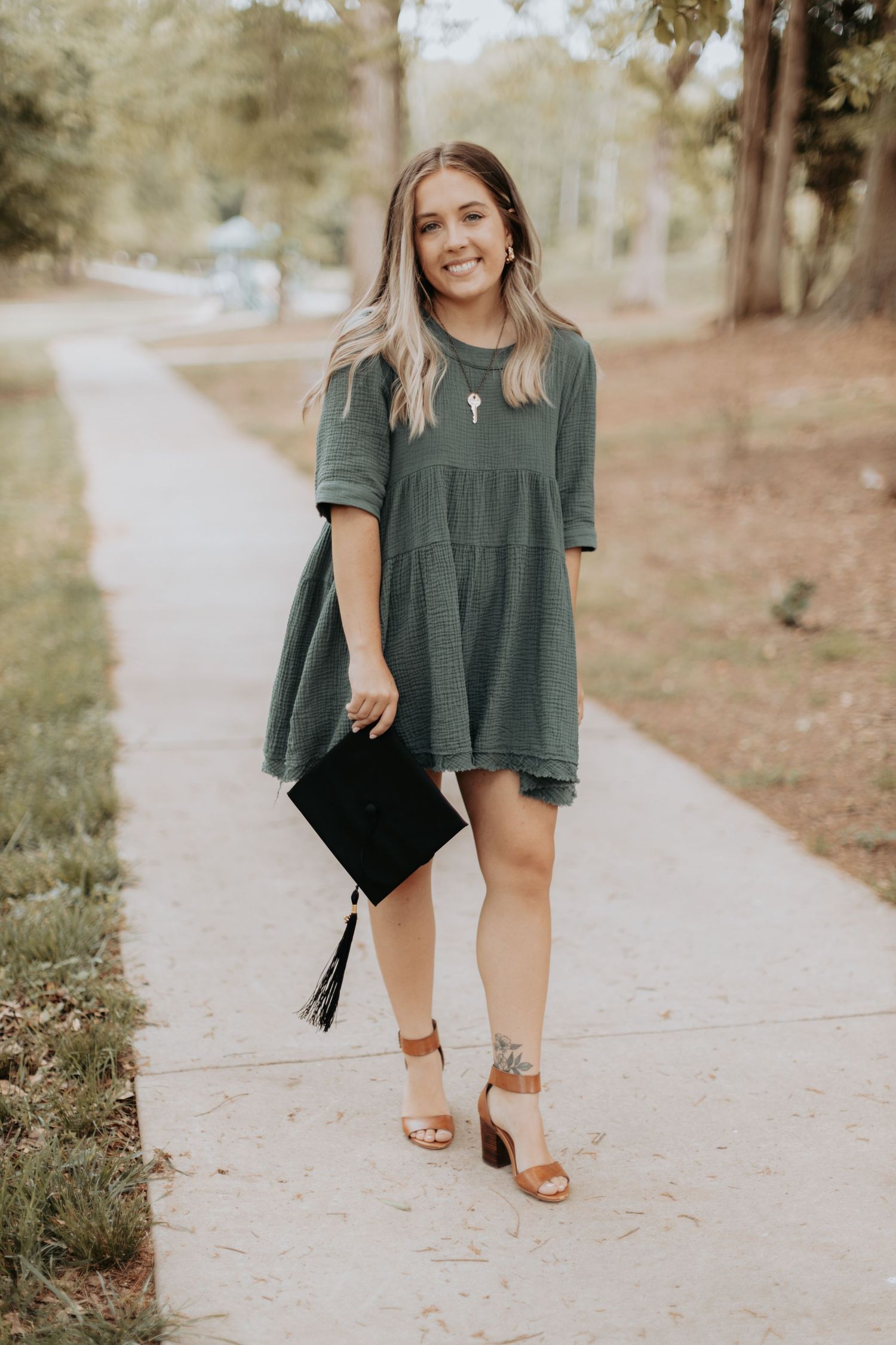 Person in a green casual dress and sandals poses outdoors on a pathway.