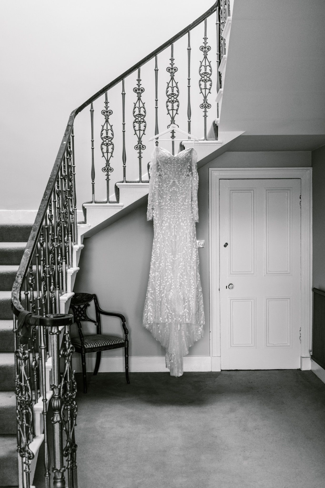 Elegant wedding dress displayed against vintage staircase with decorative iron railings.