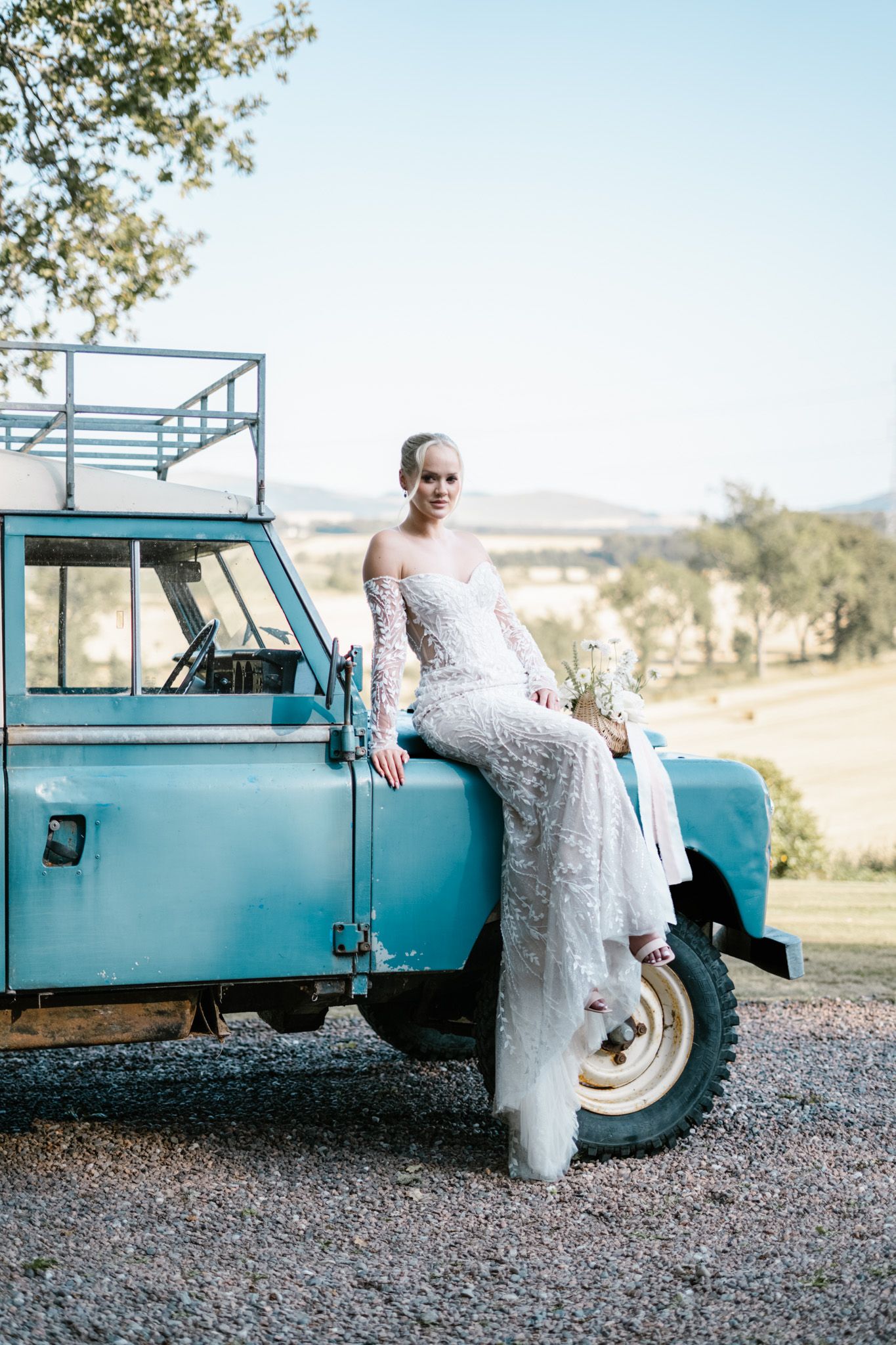 A classic turquoise Land Rover serves as a rustic backdrop for a wedding photoshoot in a countryside setting.