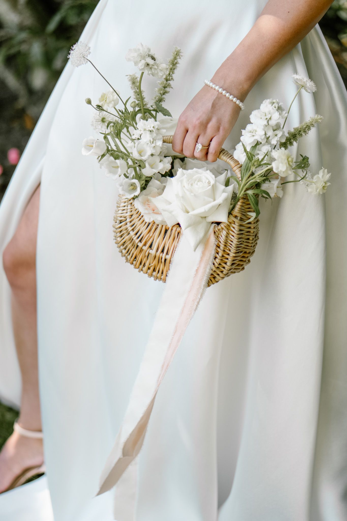 Row of white floral arrangements in wicker baskets against flowing white fabric.
